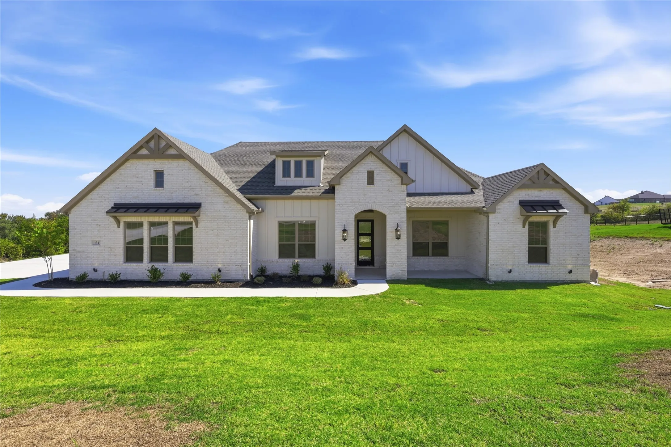 White brick exterior with dark trim accents, gabled rooflines, stone-clad entrance archway, dark-framed windows, and a paved walkway