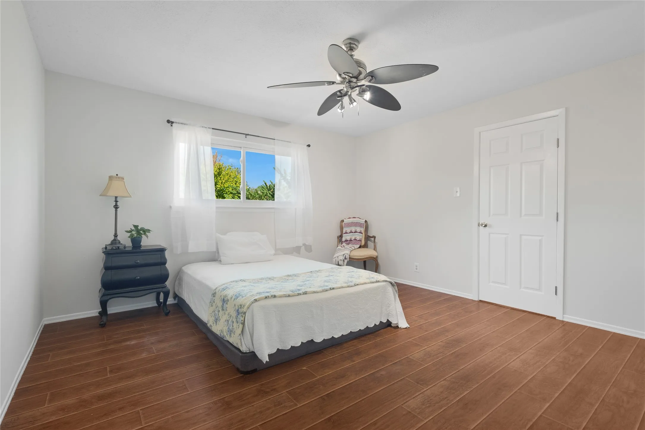Wood-finish flooring, white walls, ceiling fan with integrated lighting, and a window with natural light