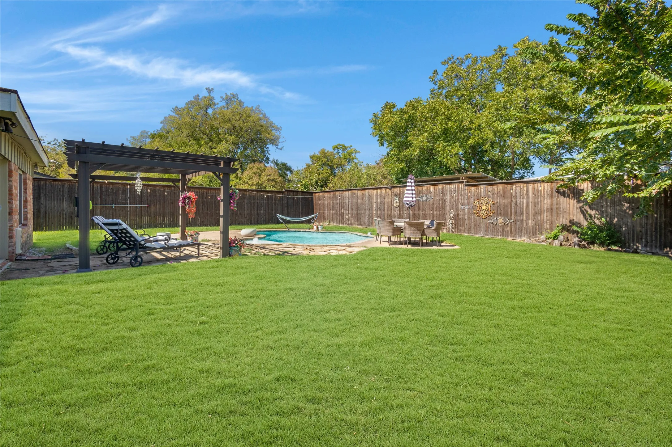 Expansive grass lawn with a swimming pool, stone paver patio, wood pergola, and wood privacy fencing