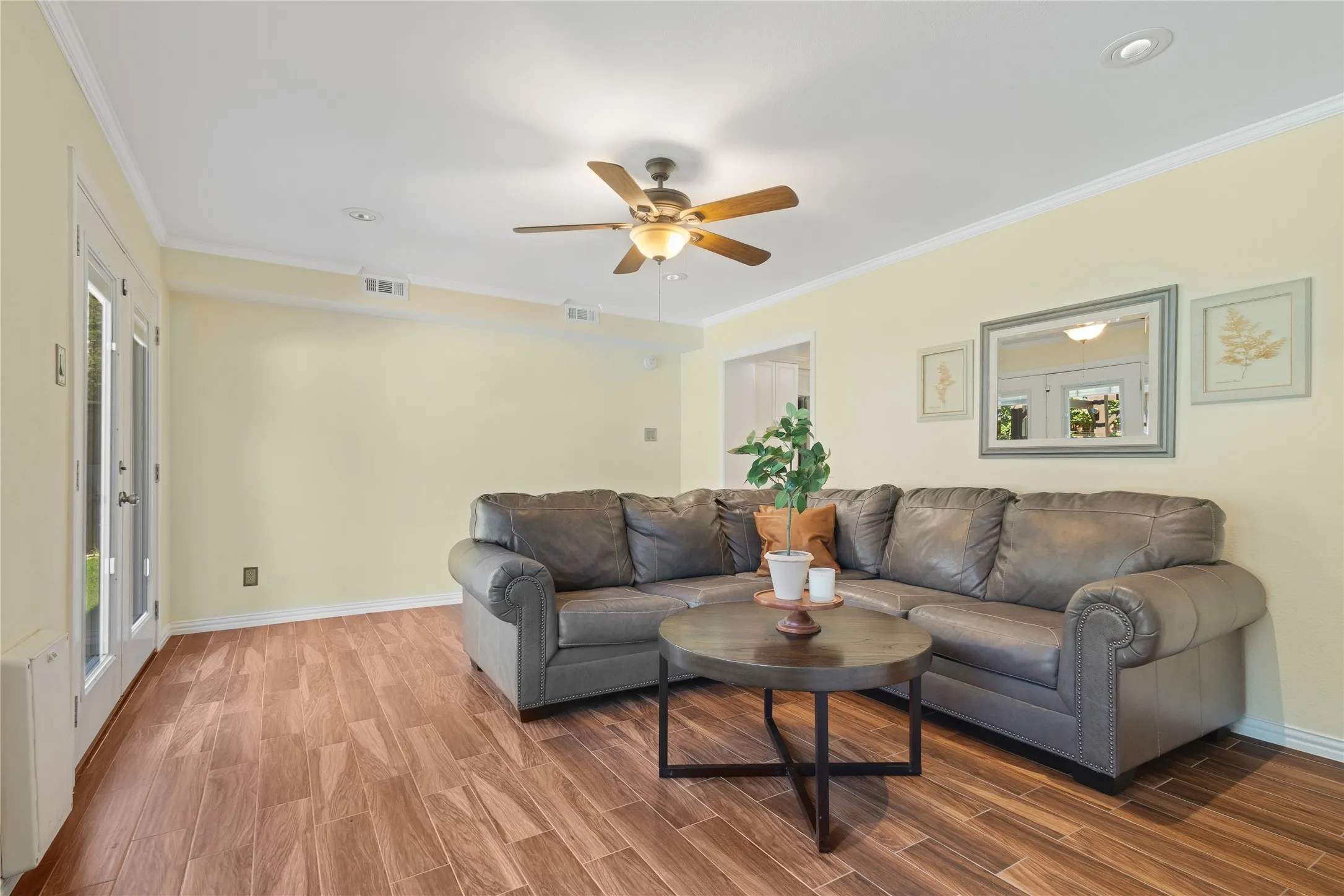 Wood-finish flooring, ceiling fan with integrated lighting, recessed lighting, crown molding, and double glass-paneled doors