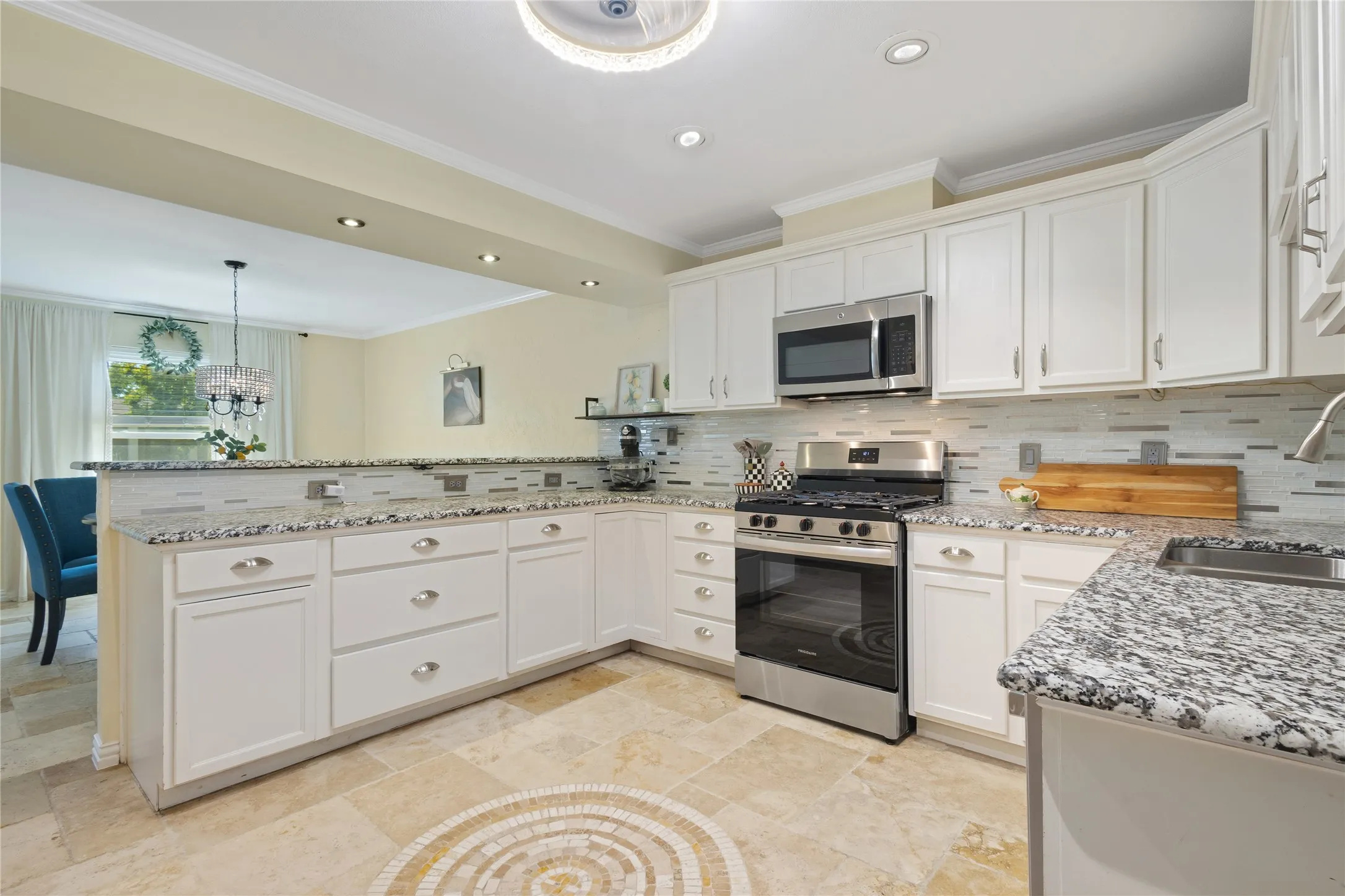White cabinetry, granite countertops, stainless steel appliances, mosaic tile backsplash, and tile flooring with a decorative inlay