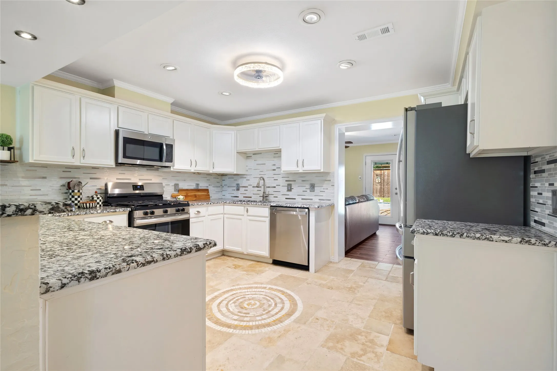 White cabinetry, natural stone countertops, stainless steel appliances, mosaic tile backsplash, and recessed lighting