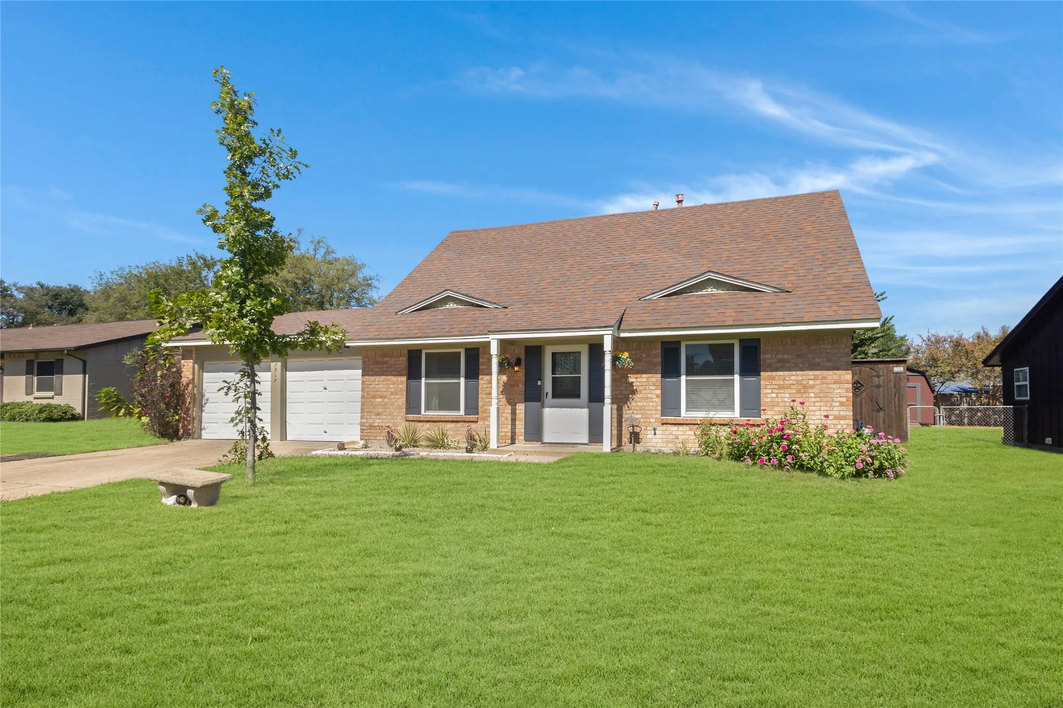 Brick exterior with a brown shingle roof, attached two-car garage, and a lush green lawn