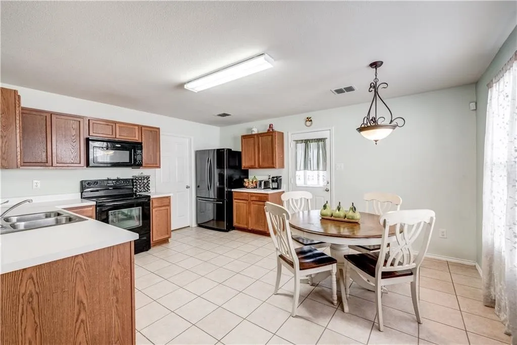 Kitchen featuring wood-finish cabinetry, black appliances, white countertops, and tile flooring