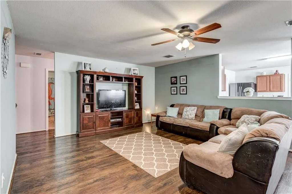 Expansive living area featuring wood-finish flooring, a ceiling fan with integrated lighting, and a built-in entertainment center