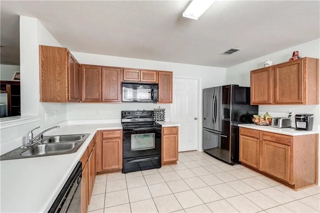Kitchen featuring wood cabinetry, white countertops, stainless steel double basin sink, black appliances, and tile flooring
