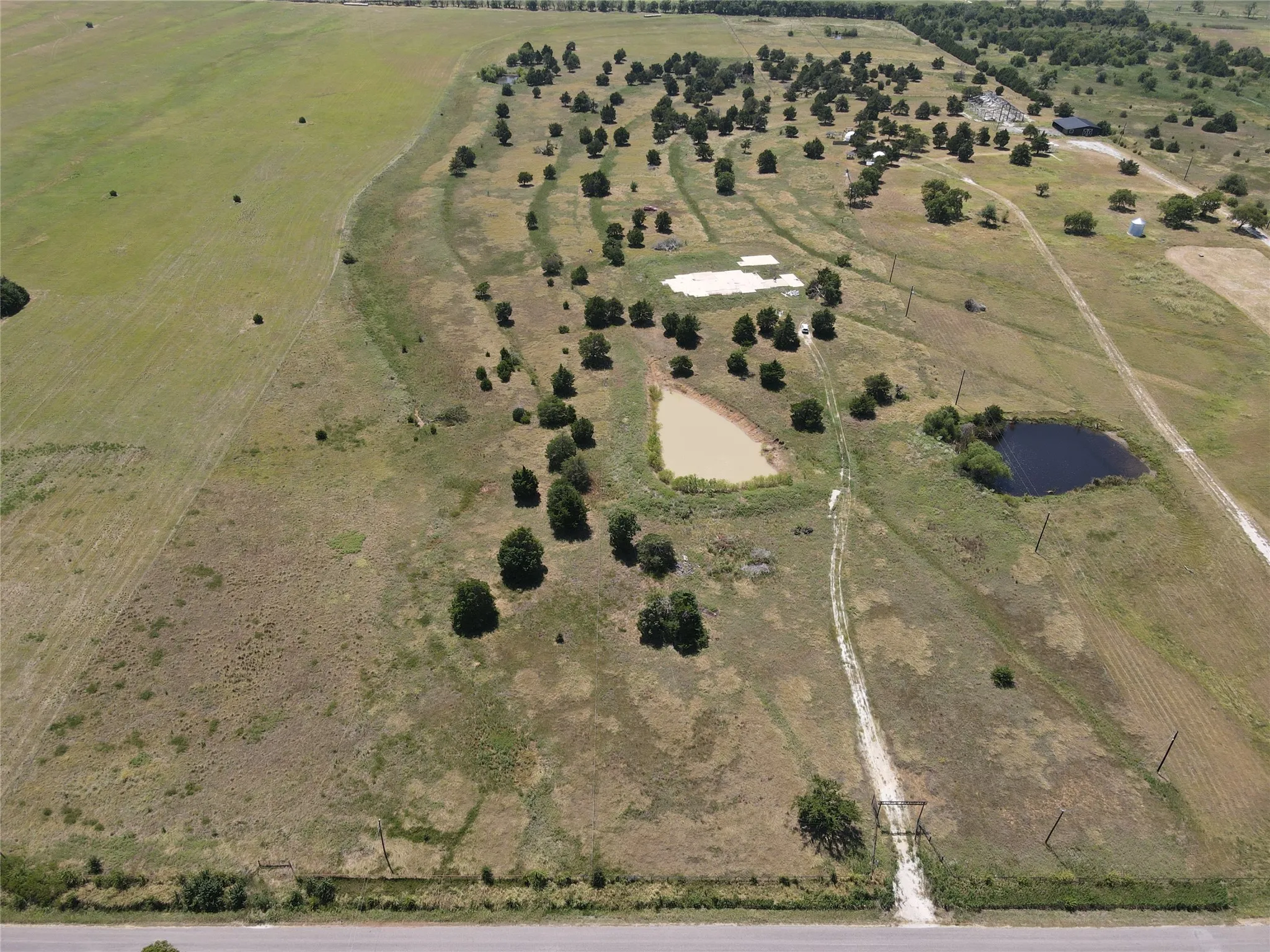 Expansive rural property featuring multiple ponds, scattered mature trees, open fields, and established unpaved access paths