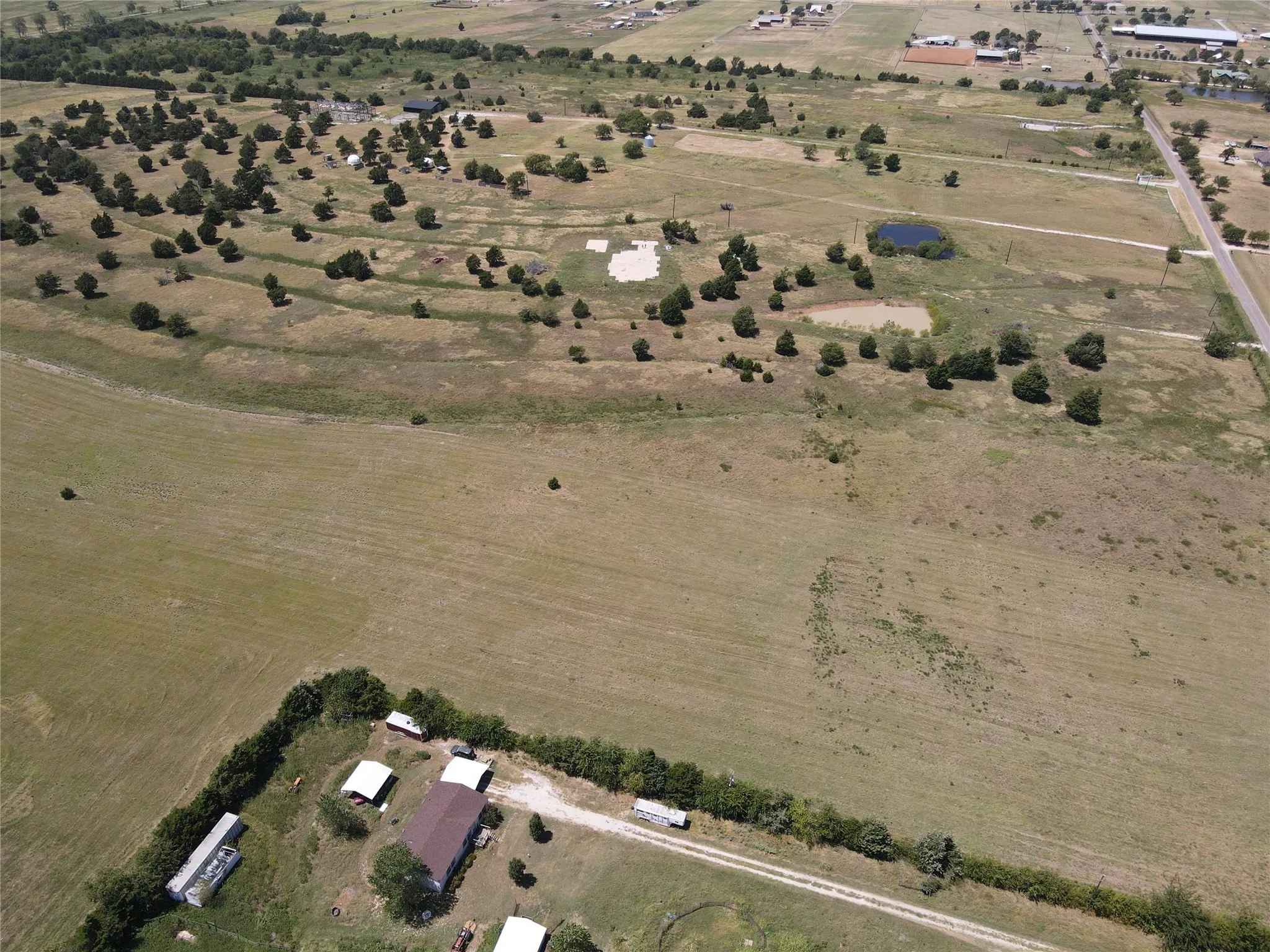 Expansive rural property featuring a main structure, multiple ancillary buildings, a gravel driveway, and a natural pond