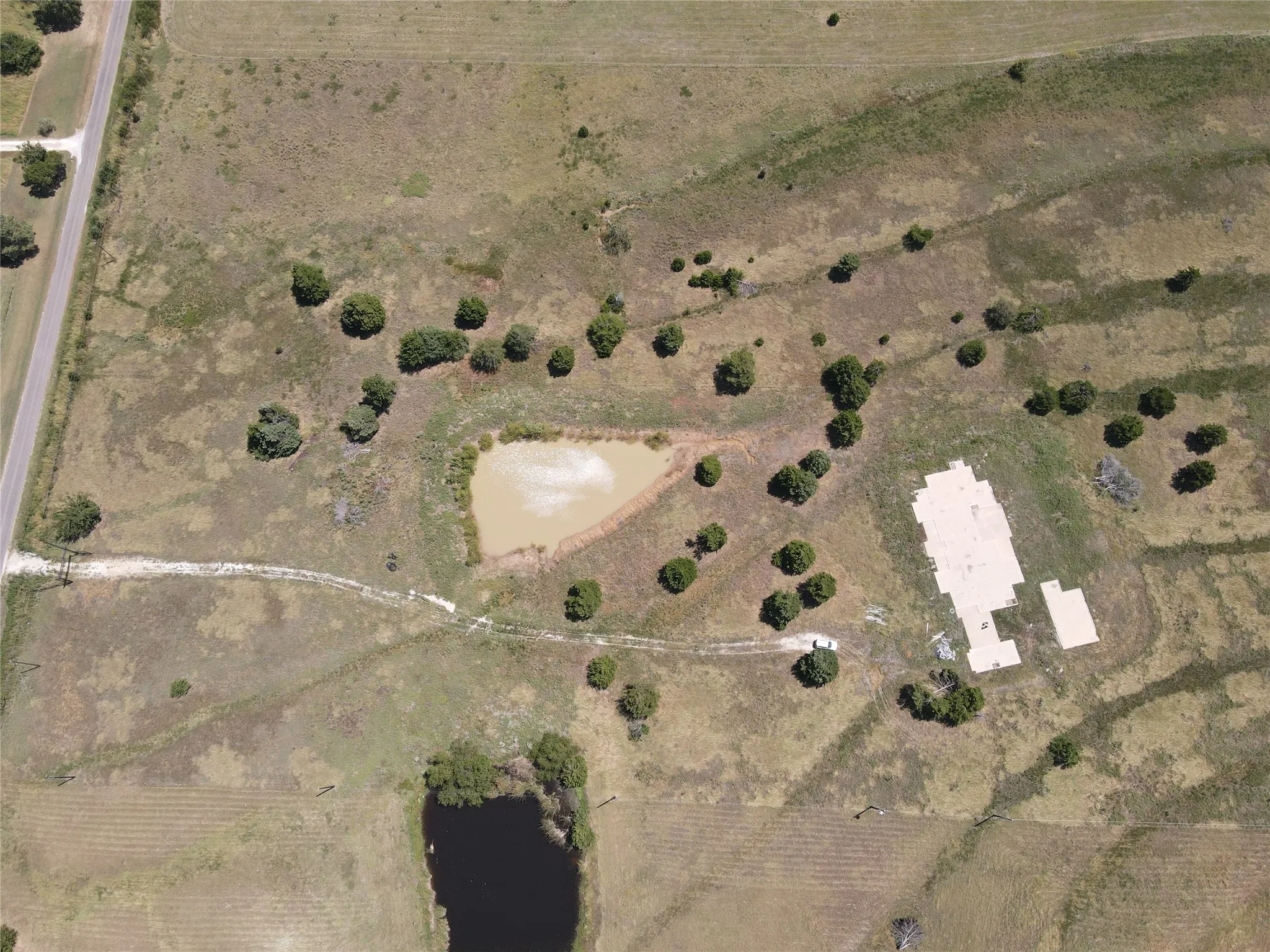 Expansive property featuring a paved road, two distinct ponds, mature trees, and a concrete foundation