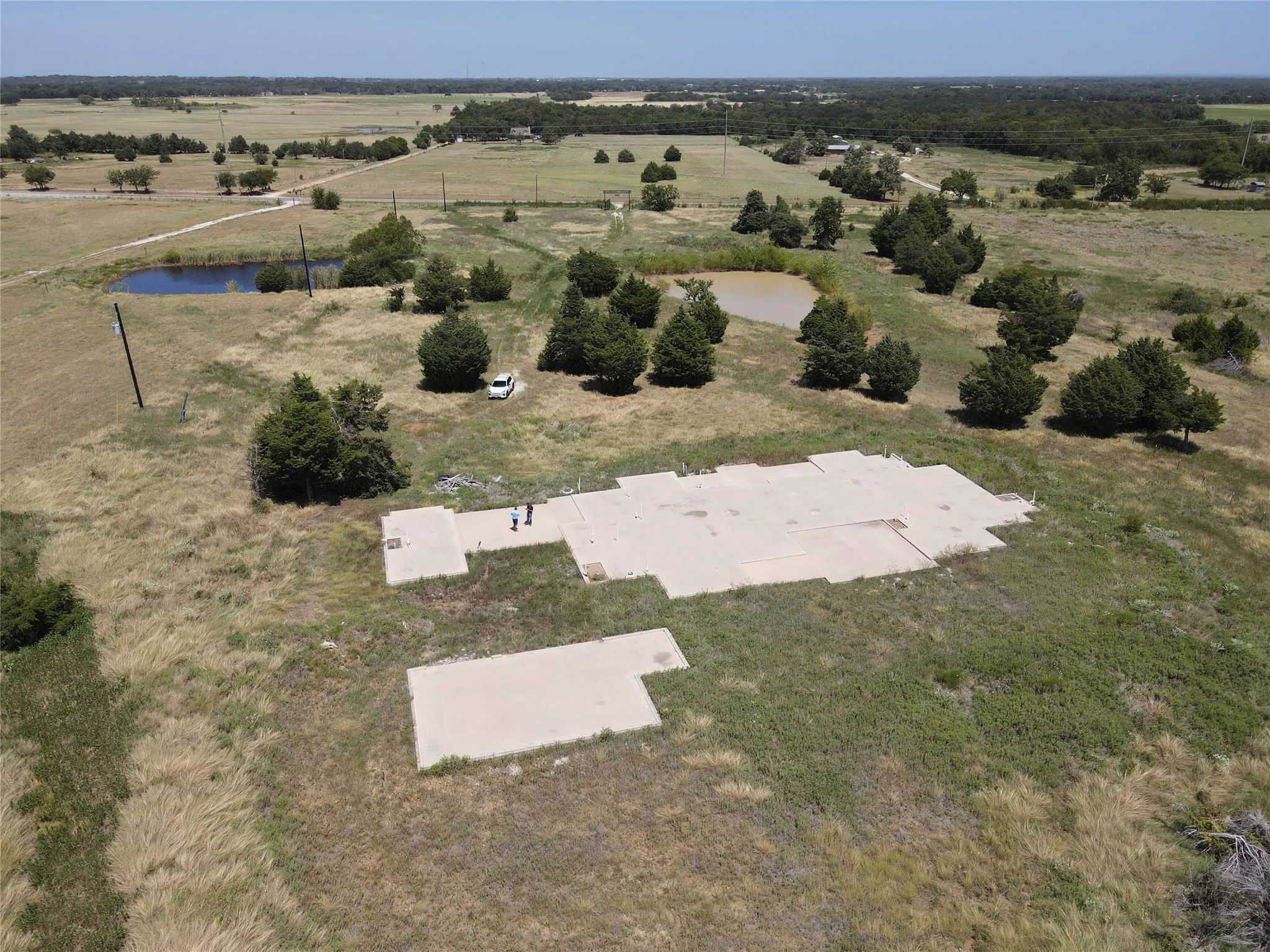 Expansive land parcel featuring multiple concrete pads, two natural ponds, mature trees, and open fields