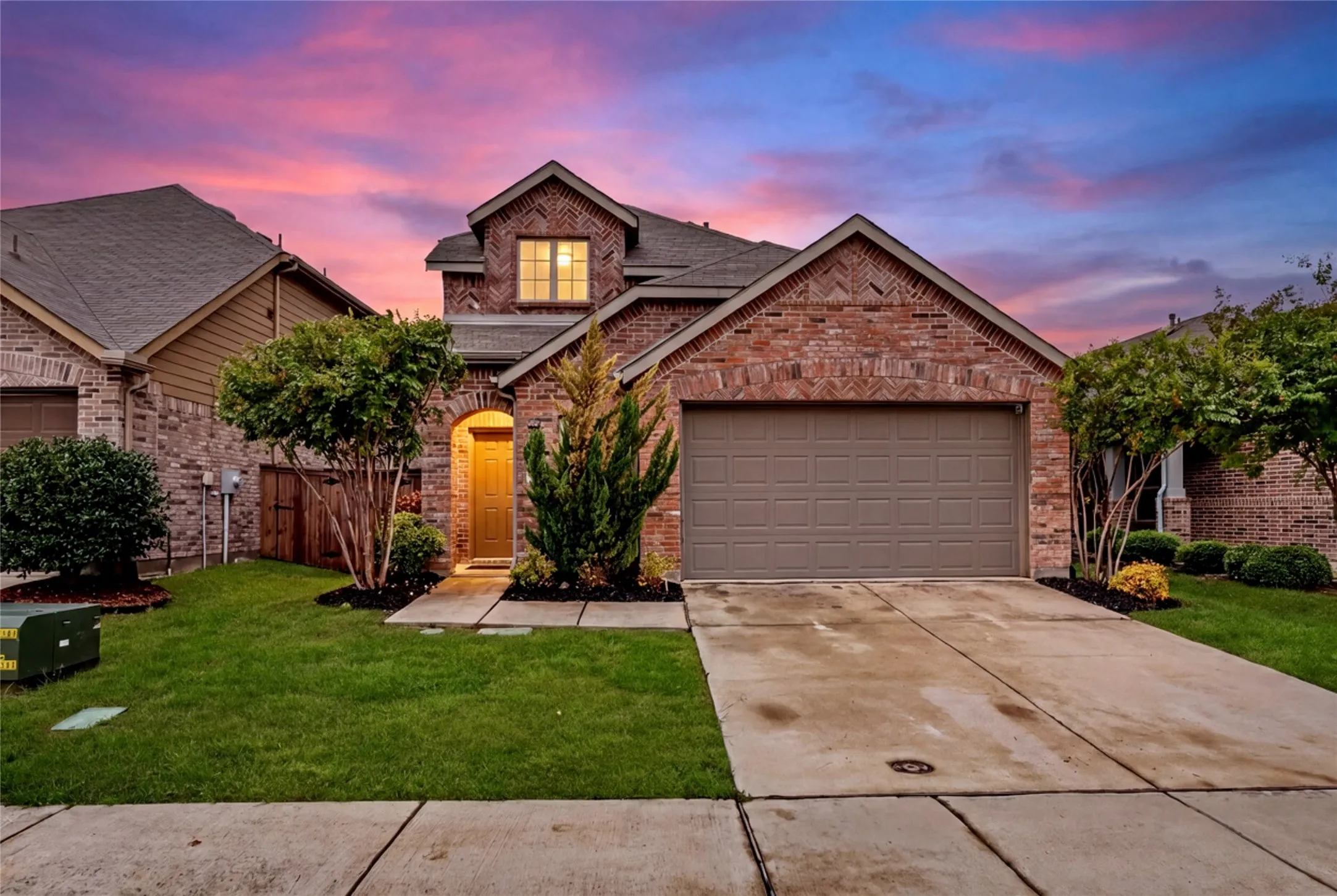 Brick facade with an arched entry, mature landscaping, and an attached garage
