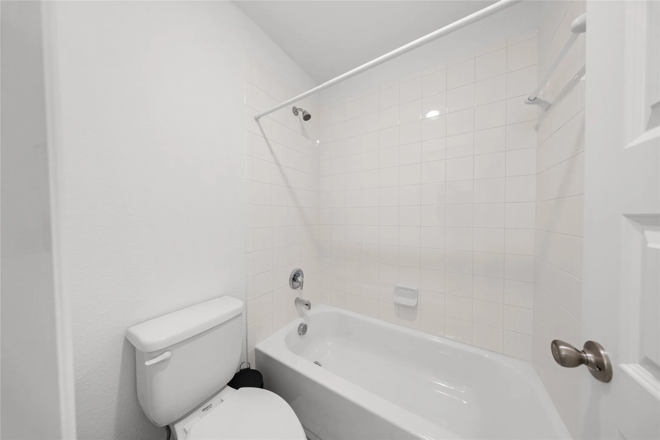 White tile shower surround, complete with a tub and shower combination, and a toilet