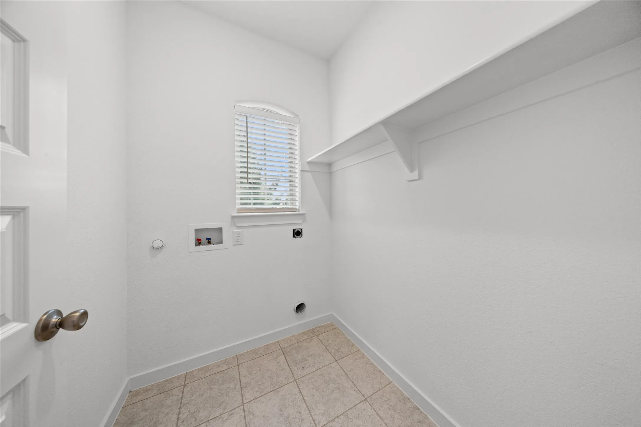 Utility room featuring tile flooring, a window with blinds, and an integrated storage shelf