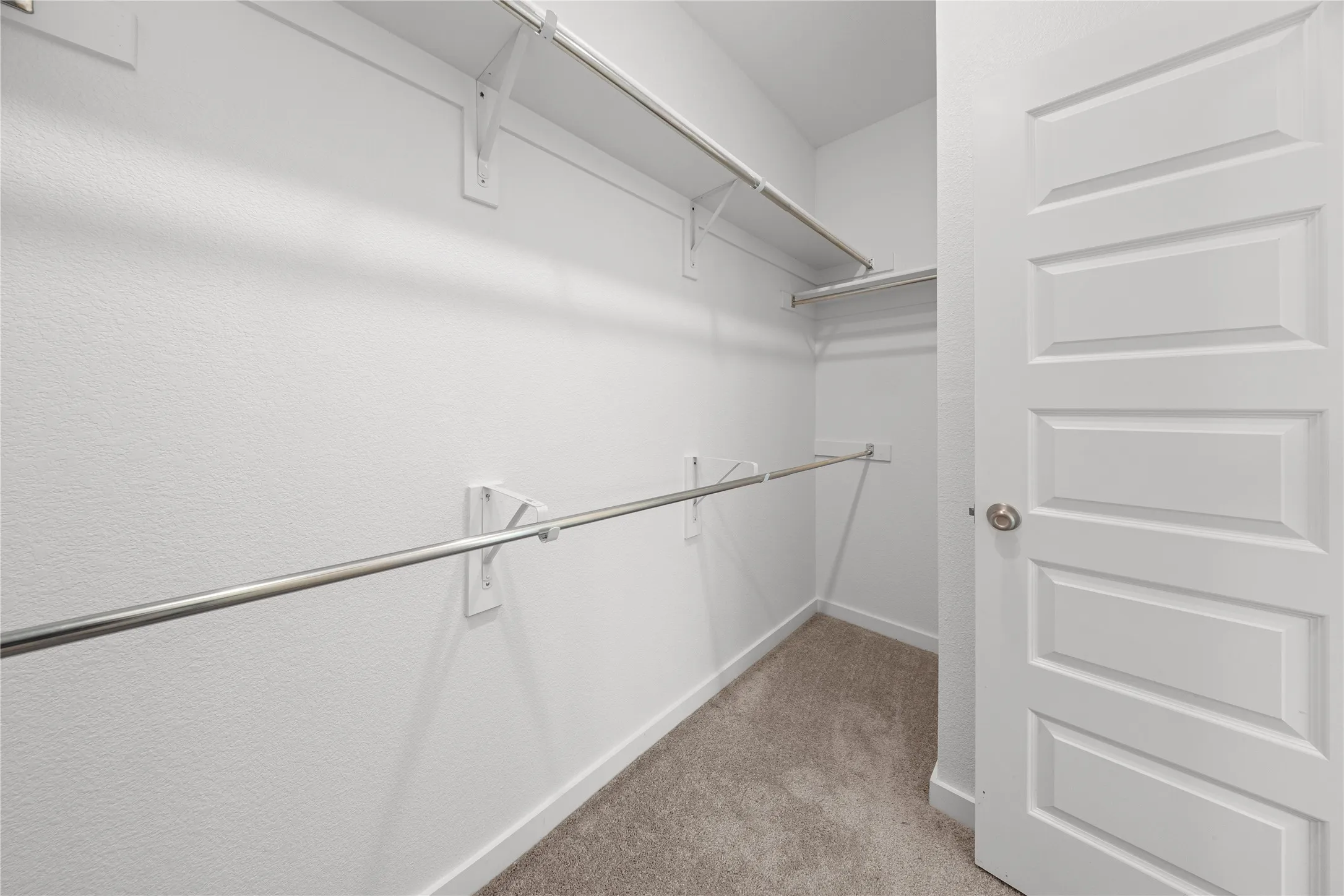 Walk-in closet featuring white painted walls, chrome hanging rods, white shelving, and a paneled white door