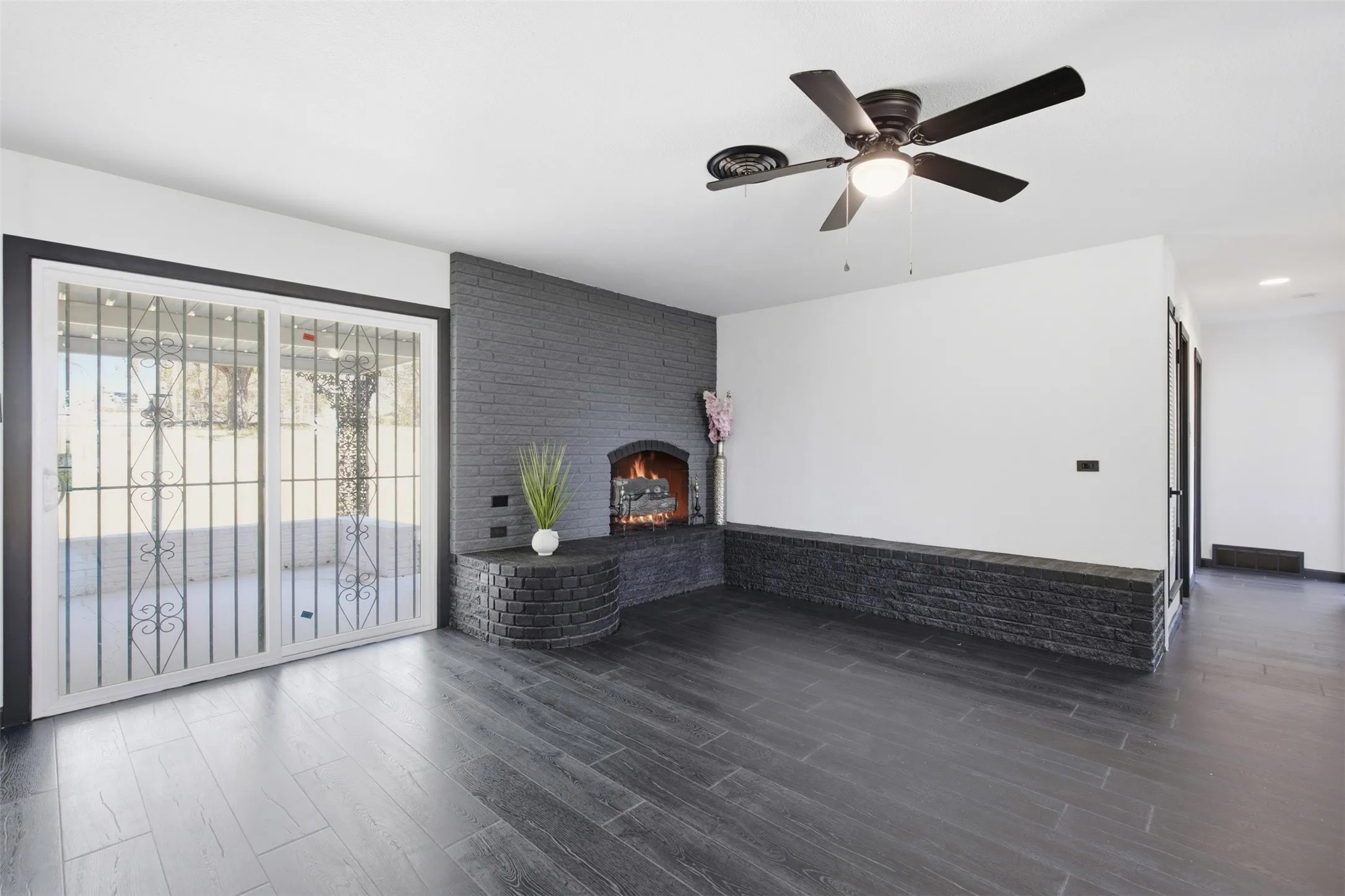 Spacious living area featuring a fireplace, dark wood-finish flooring, and a ceiling fan with integrated lighting