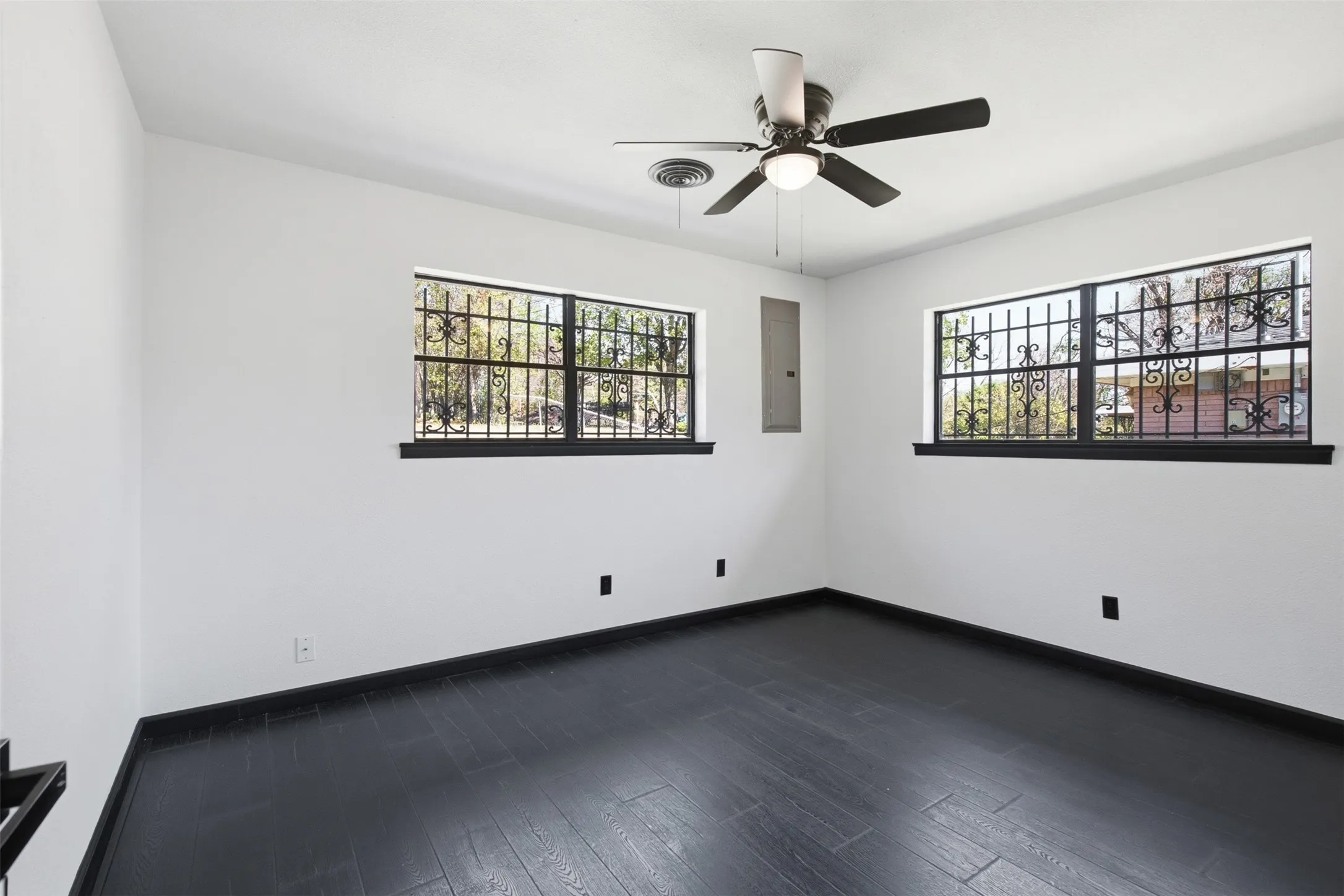 Dark wood-finish flooring, white walls, and two windows with decorative security grilles