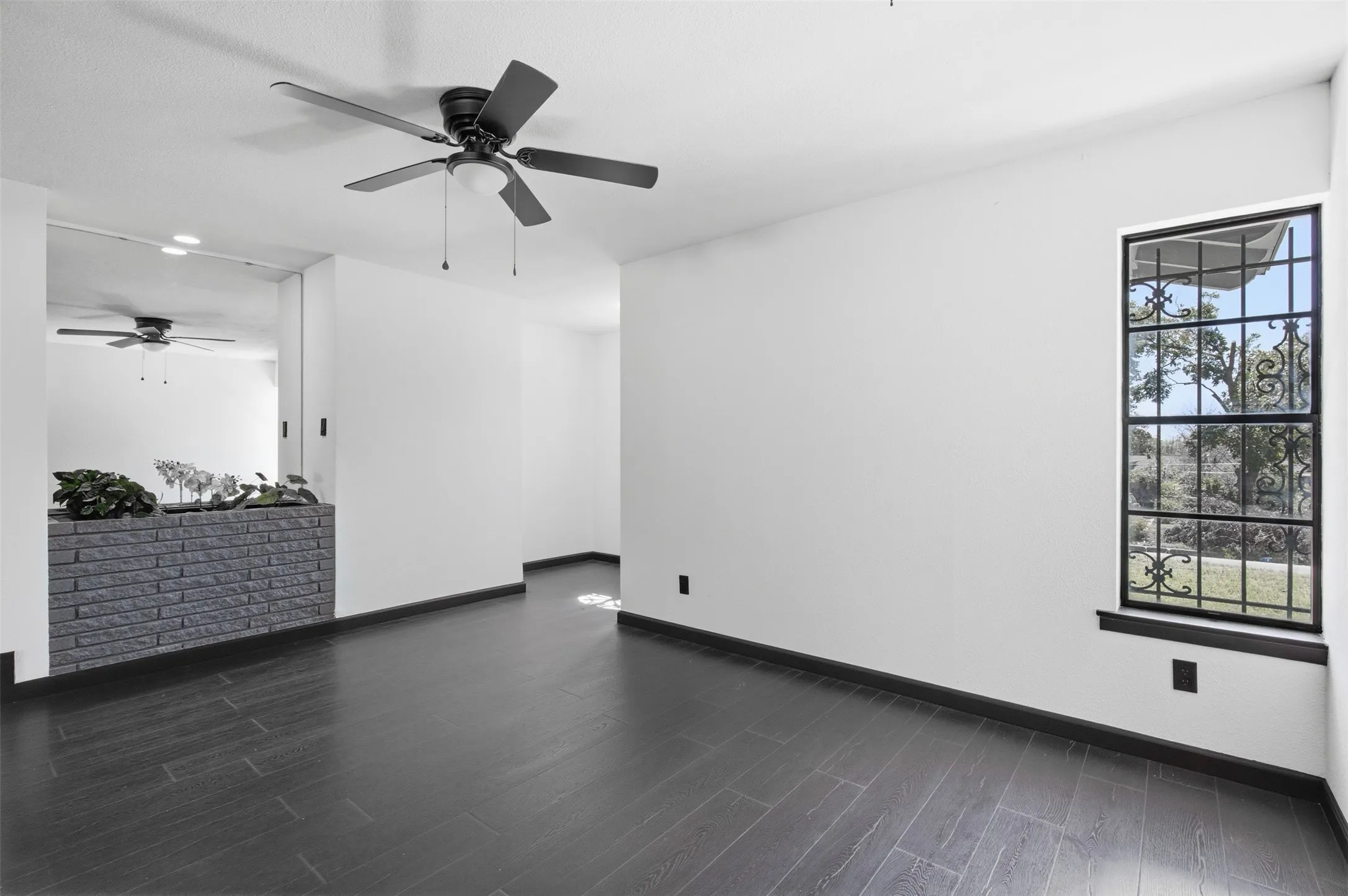 Dark wood-finish flooring, white walls, black ceiling fan, black window trim, and a decorative security grill
