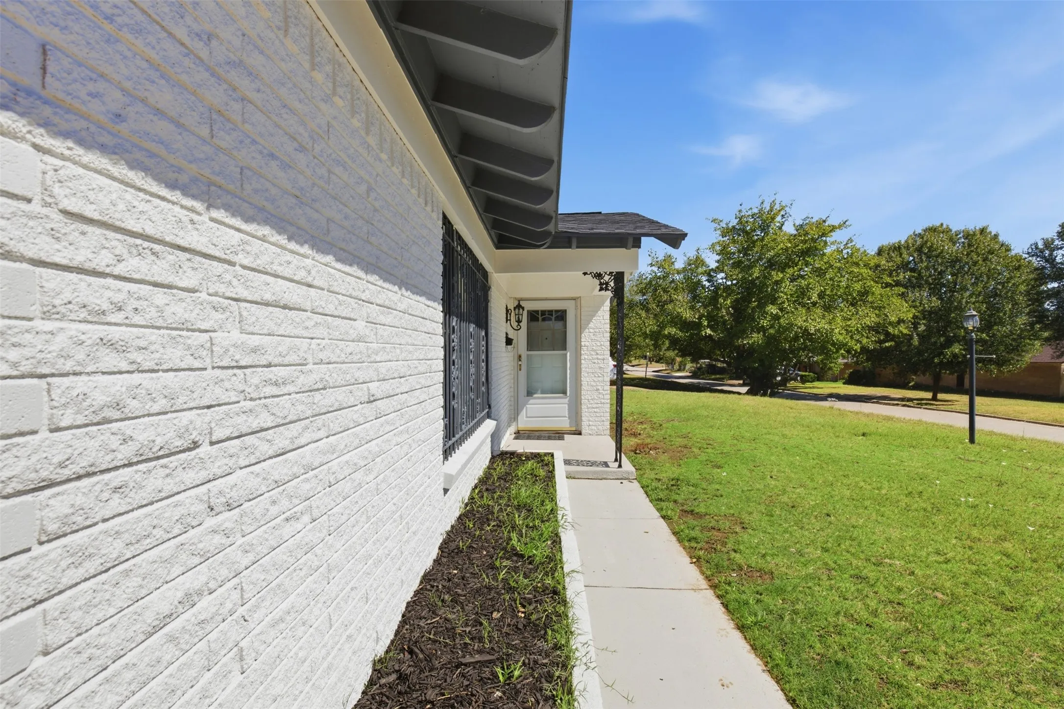 White brick exterior, black wrought iron window security bars, covered entry, concrete walkway, and manicured lawn