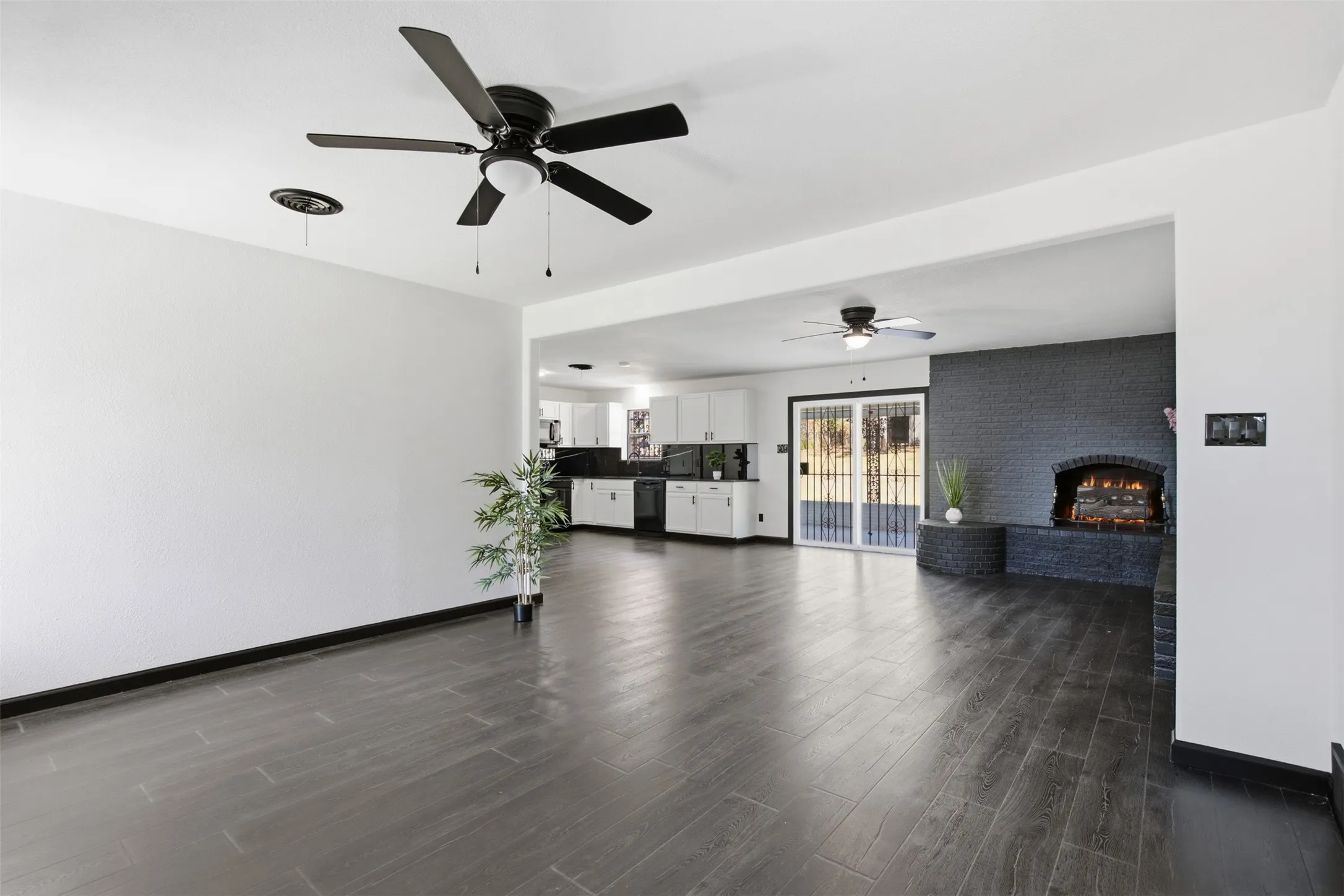Open concept living space featuring wood-finish flooring, two ceiling fans, and a brick fireplace