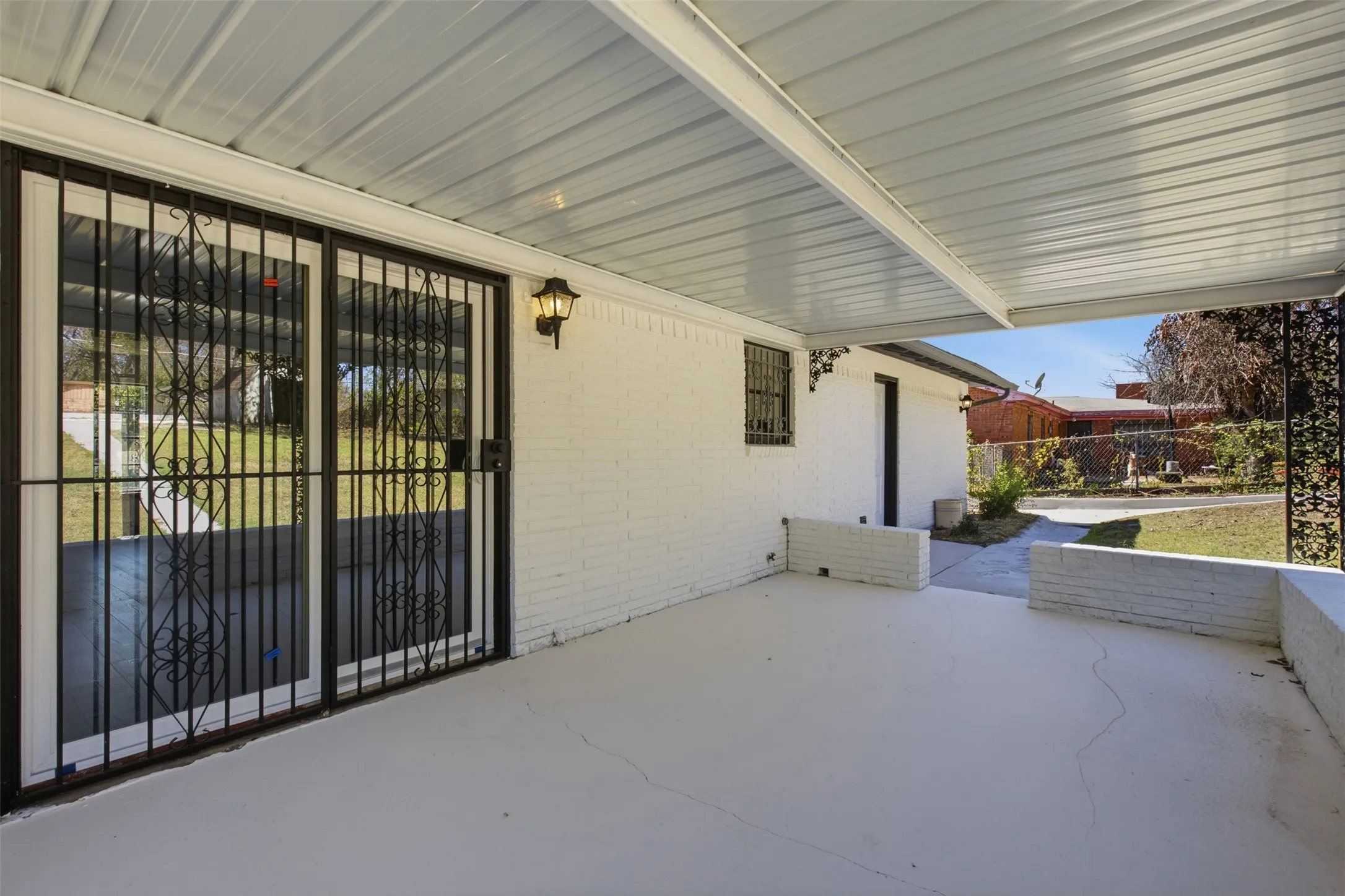 Covered patio featuring a white painted brick exterior, outdoor wall sconce, and sliding glass doors with decorative security bars