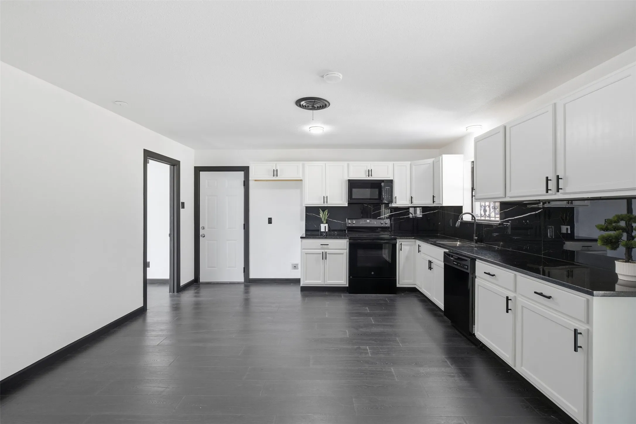 Open-concept kitchen featuring white cabinetry, dark countertops, dark appliances, and dark wood-finish flooring