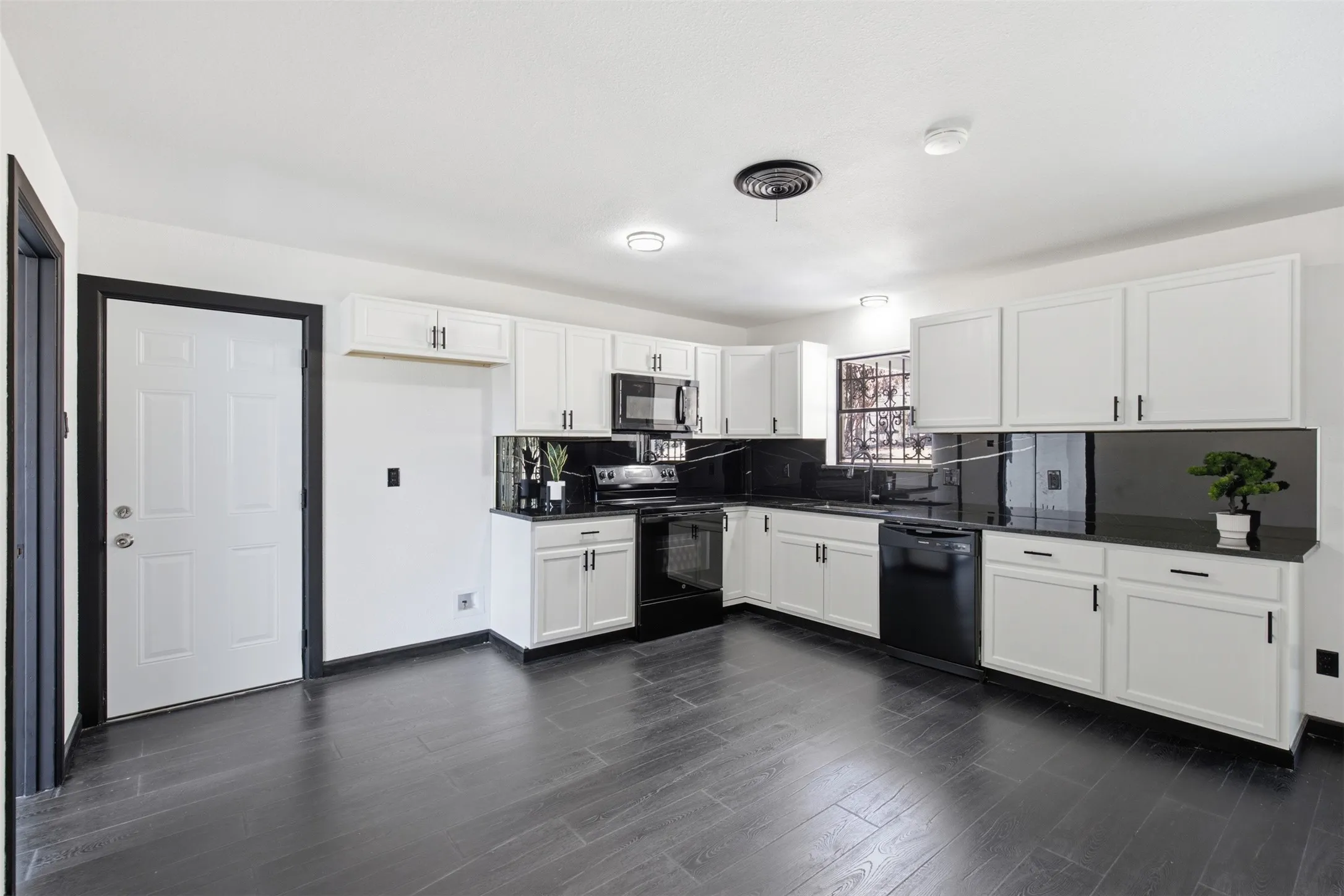 Kitchen featuring white cabinetry, dark countertops, dark backsplash, a built-in dishwasher, and wood-finish flooring