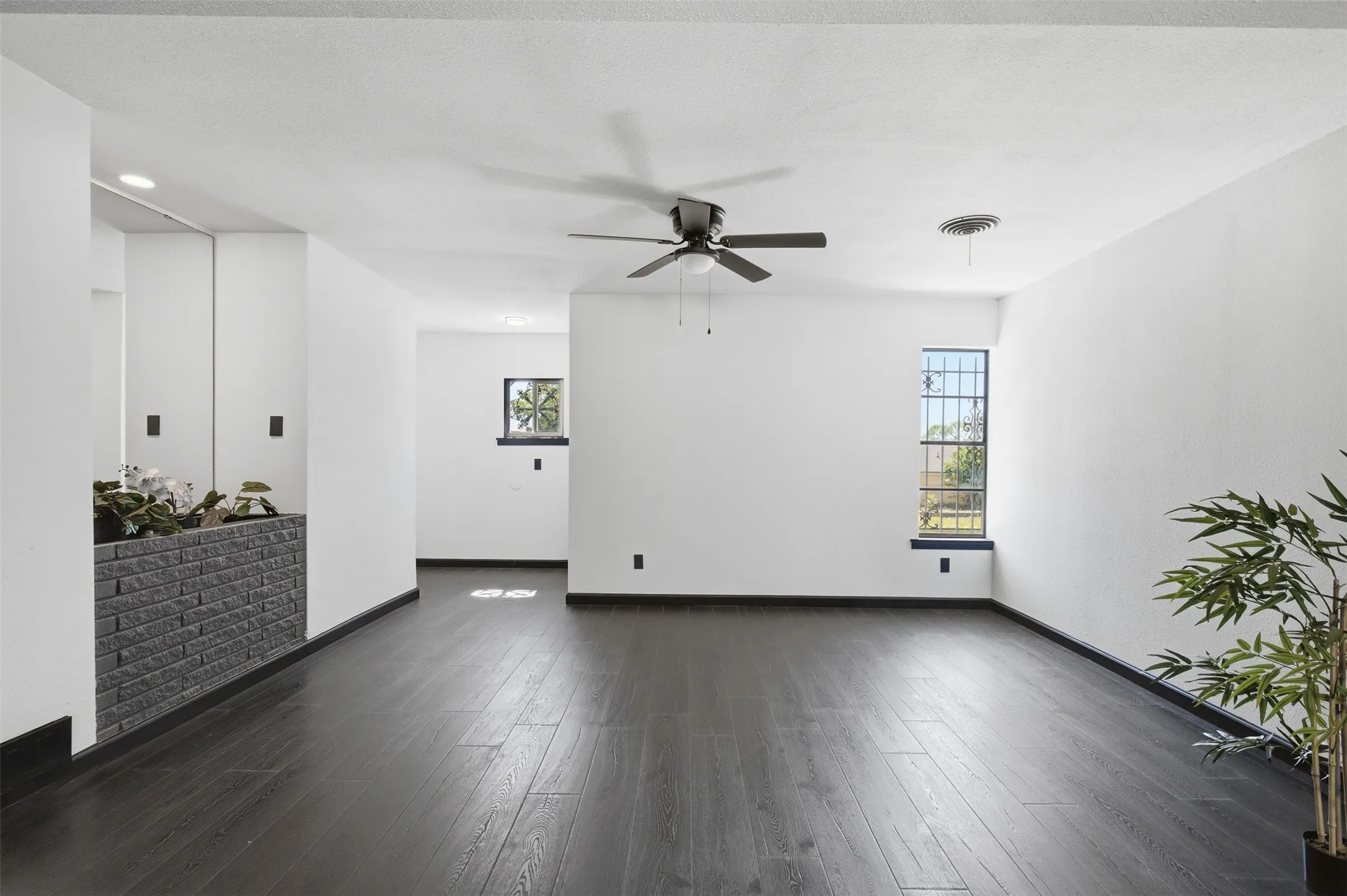 Dark wood-finish flooring, white painted walls, and a ceiling fan with integrated lighting