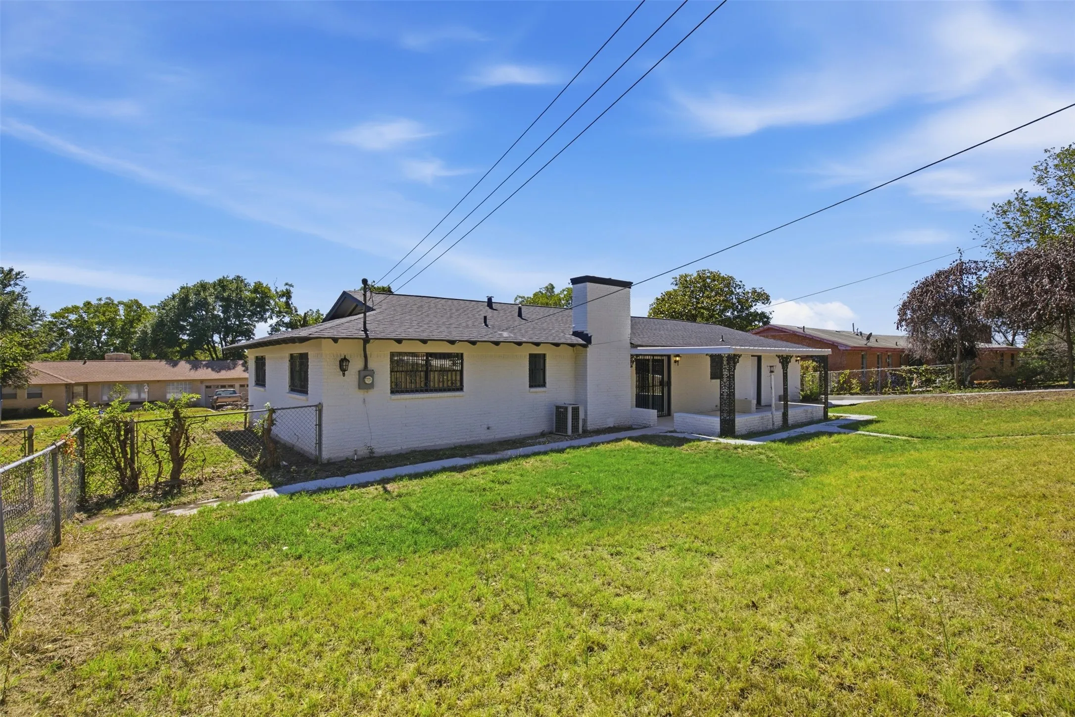 Expansive grassy yard with chain-link fencing, white exterior, covered patio, and attached chimney