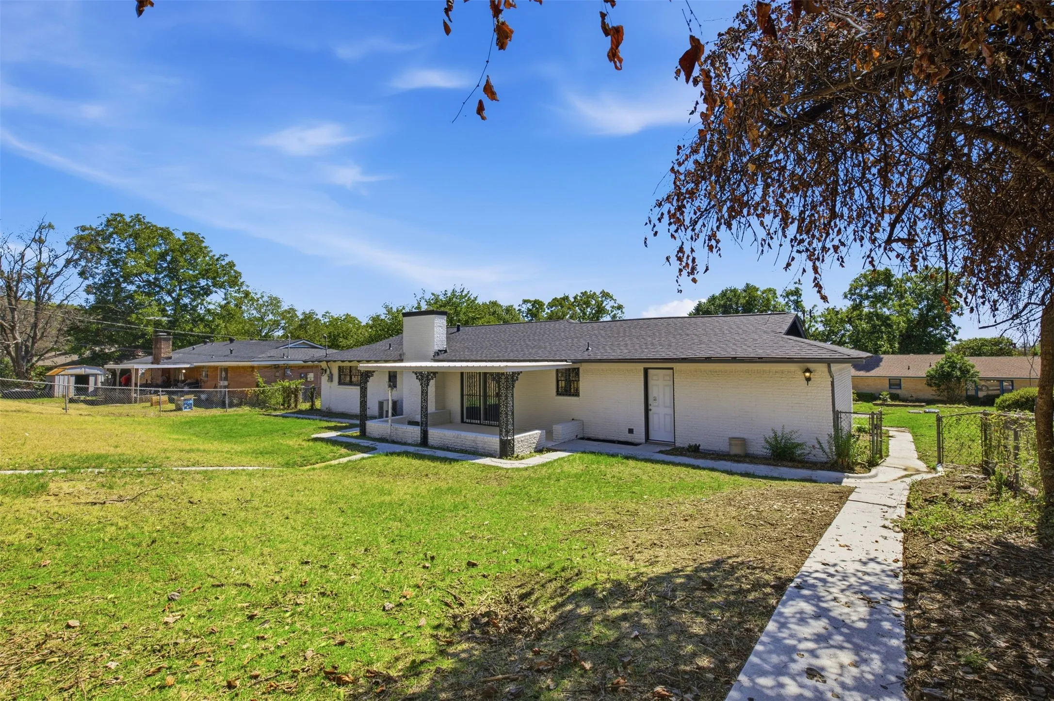 Exterior featuring white siding, a covered patio, a dark shingle roof, and a concrete pathway
