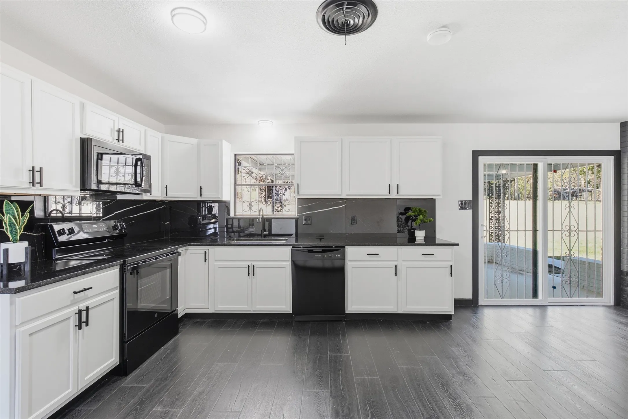 White cabinetry with dark hardware, dark stone countertops, dark backsplashes, dark wood-finish flooring, and a sliding glass door