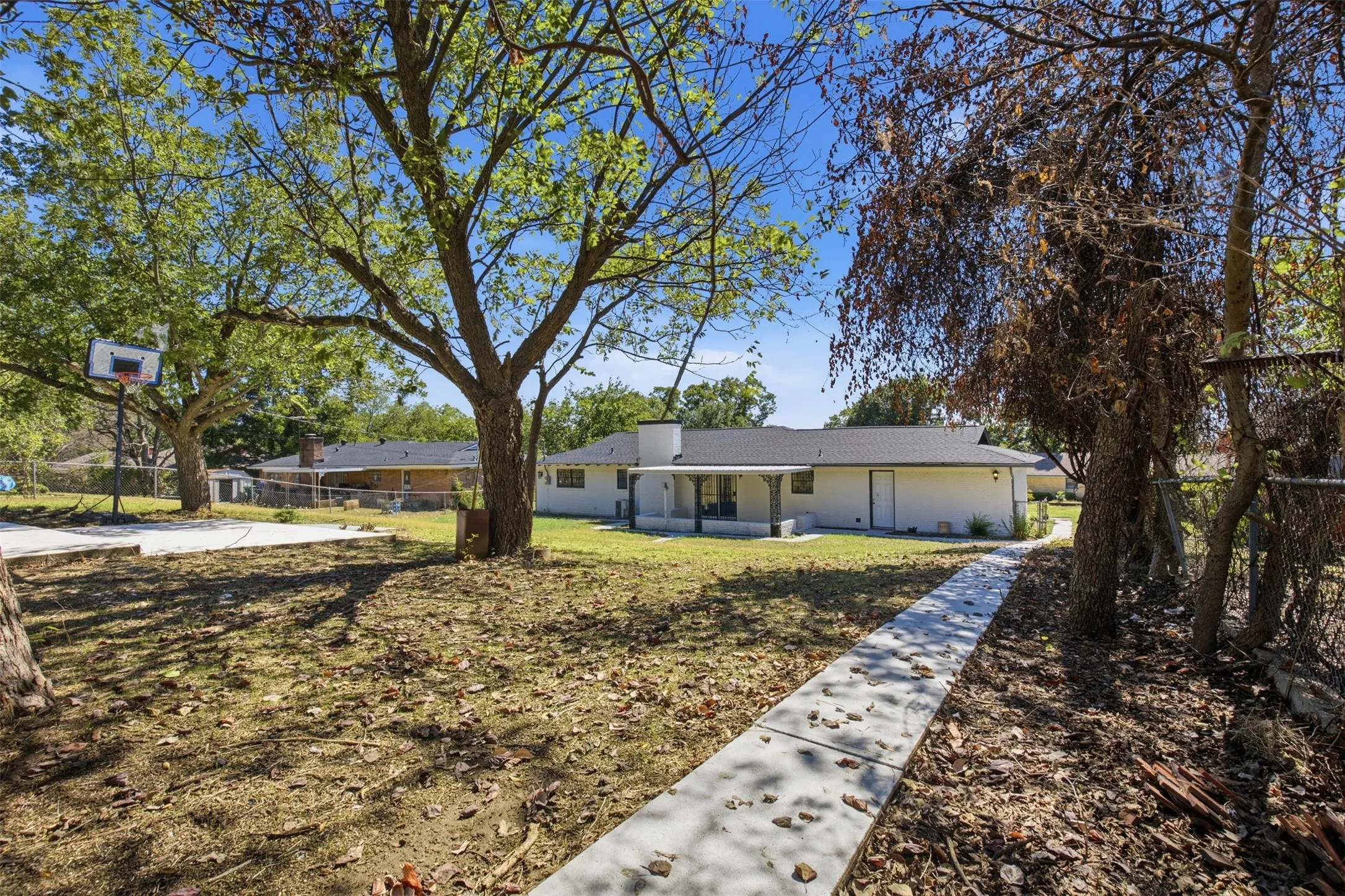 Expansive yard with mature trees, concrete pathway, and a basketball court