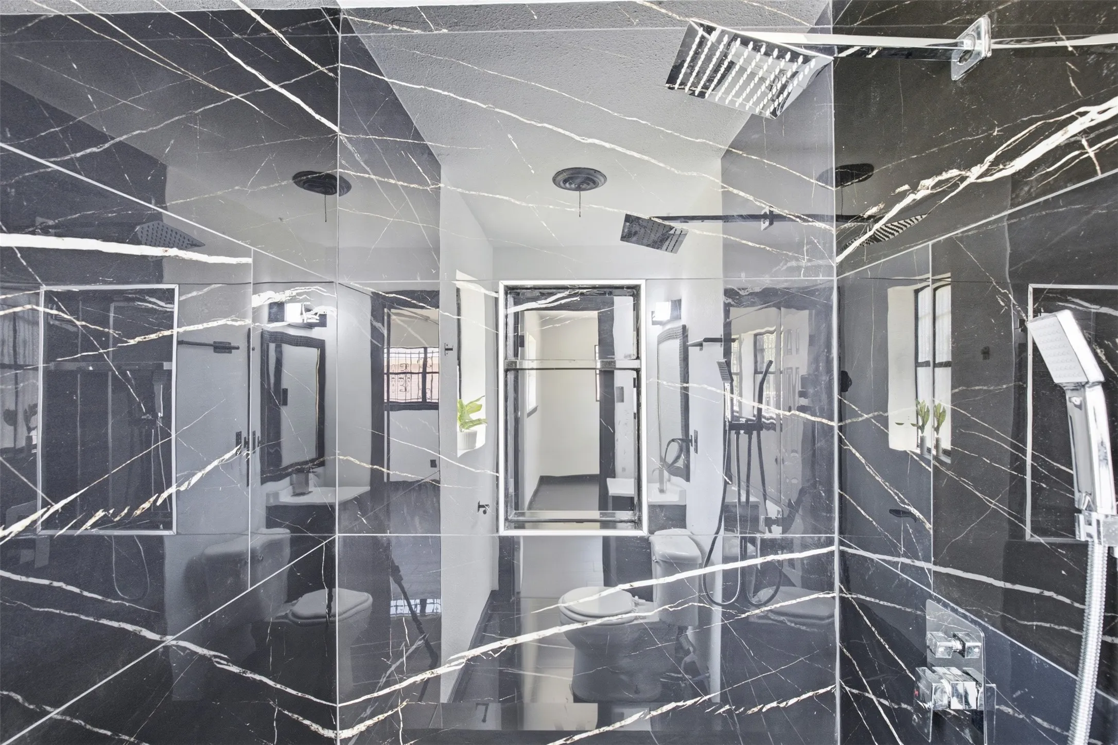 Shower enclosure featuring black marble-style tile, multiple shower heads, and an integrated handheld shower sprayer
