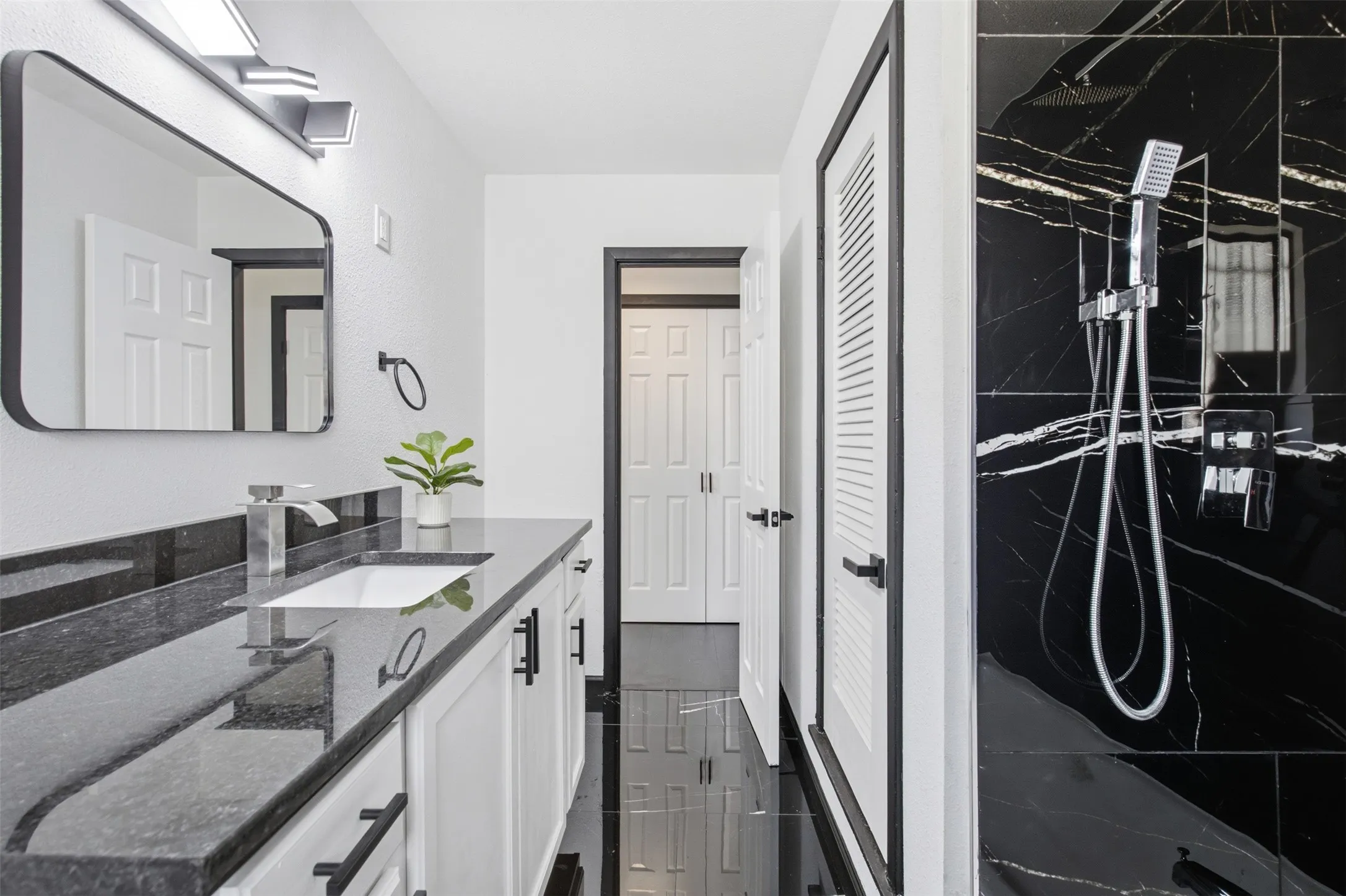 White vanity cabinetry with matte black hardware, black stone countertop, and an undermount sink