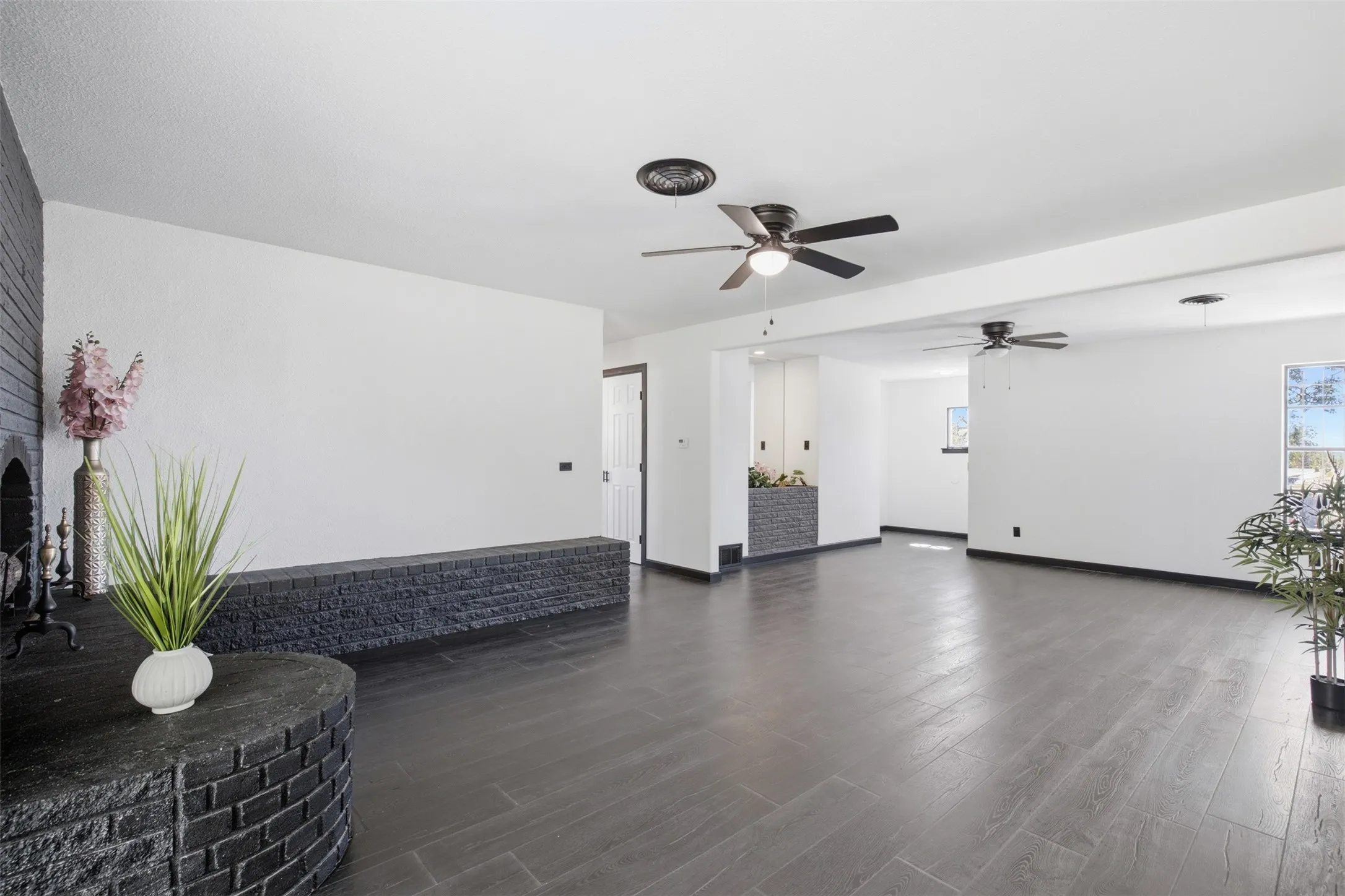 Expansive room featuring dark wood-finish flooring, white walls, and multiple ceiling fans