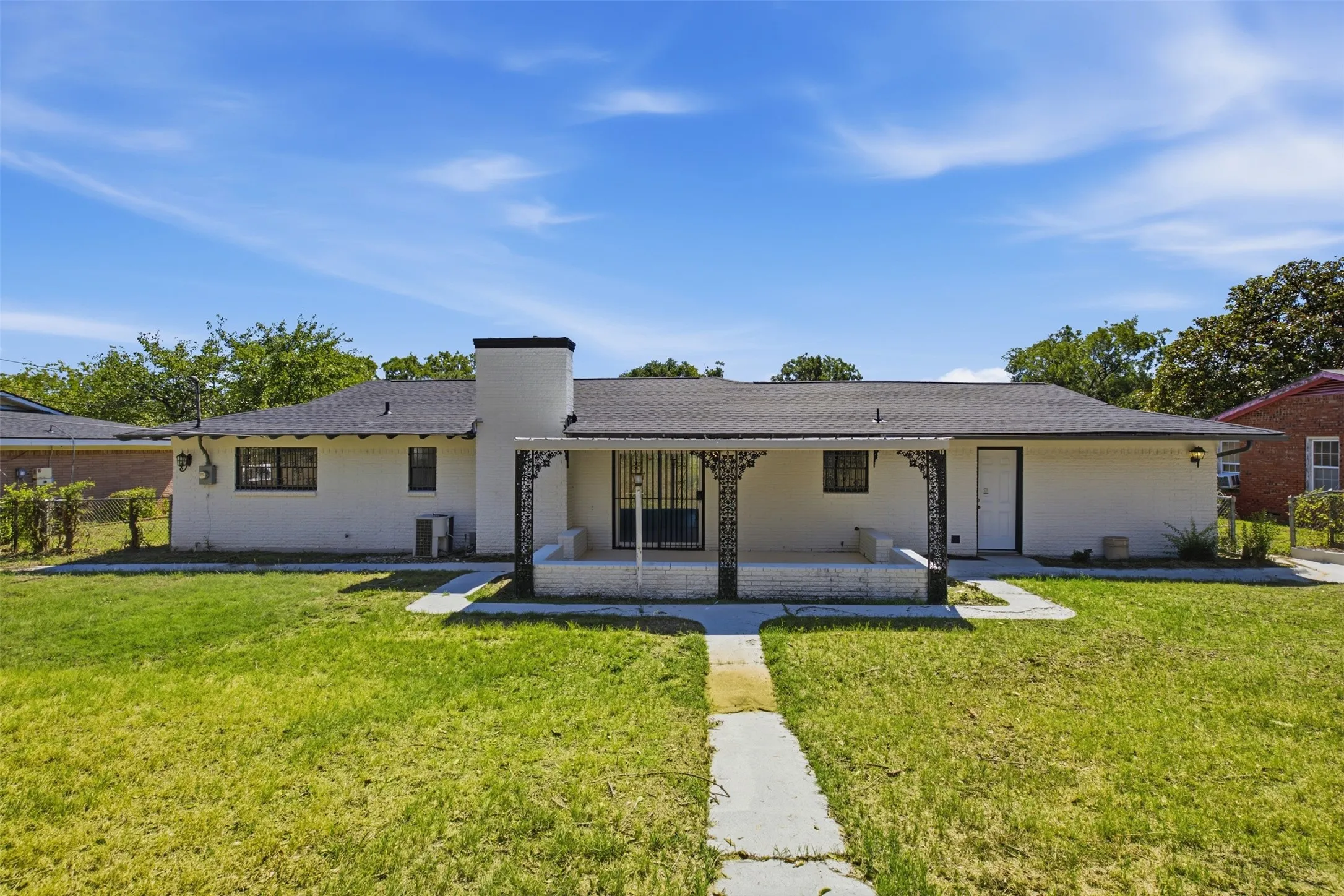 White exterior with a dark shingle roof and a covered patio featuring decorative metal columns