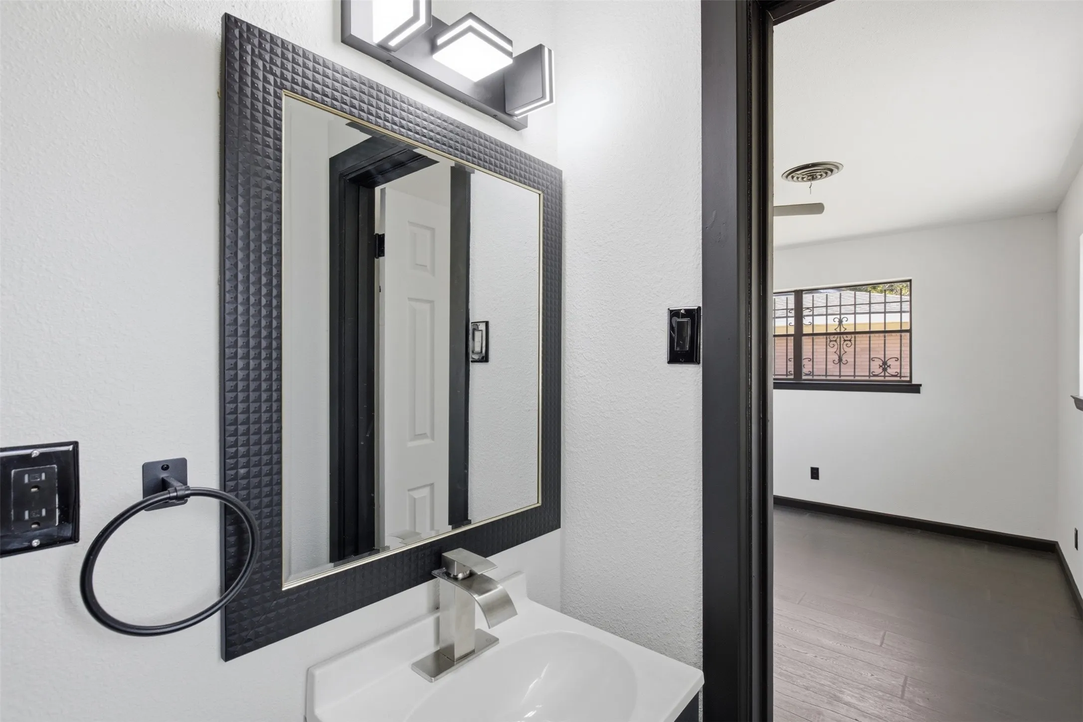 Vanity featuring a white basin sink, brushed nickel faucet, and a textured black-framed mirror
