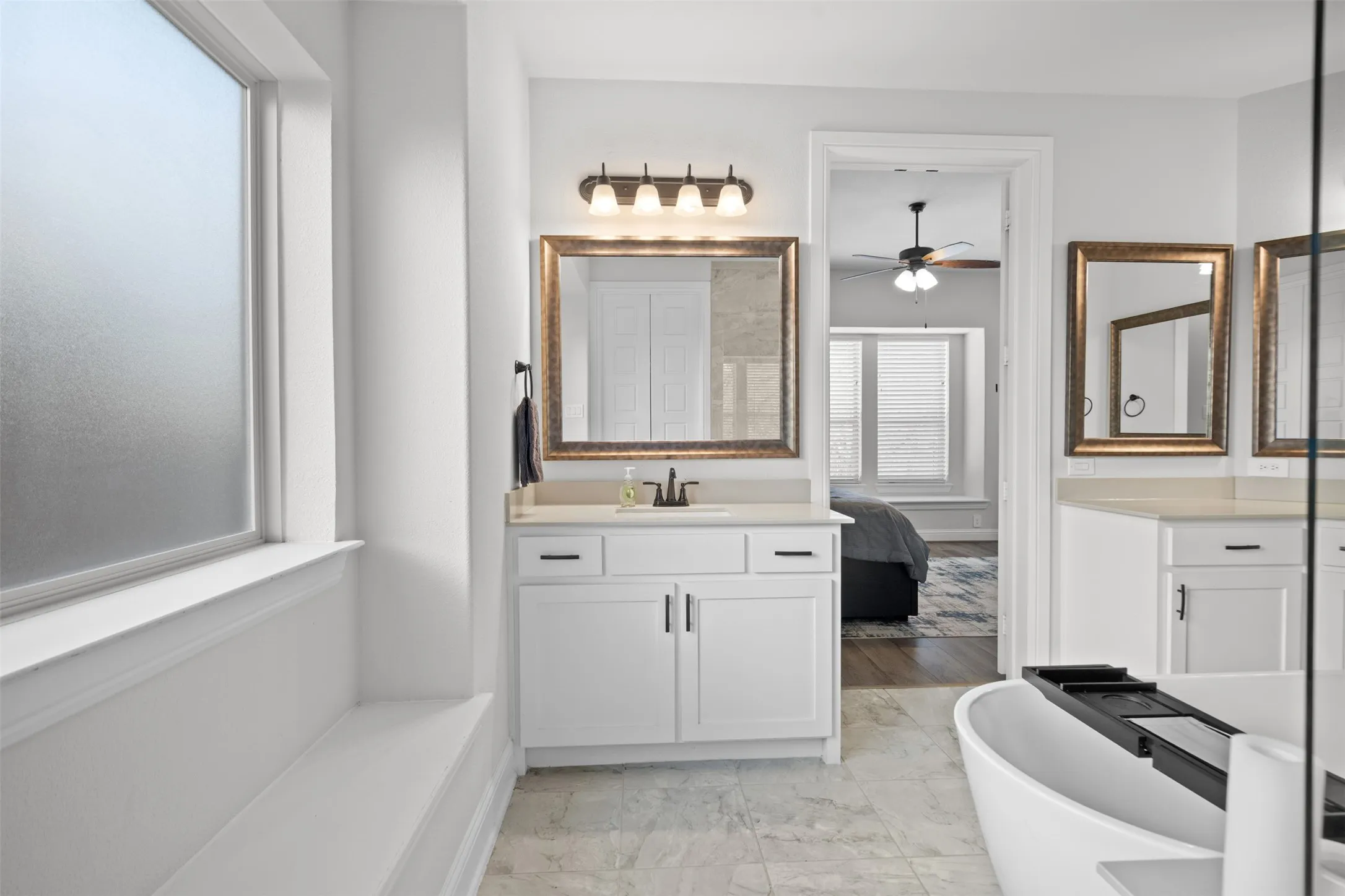 Frosted window, built-in window bench, white vanity with countertop, framed mirror, and freestanding​​‌​​​​‌​​‌‌​‌‌​​​‌‌​‌​‌​‌​​​‌​​ bathtub