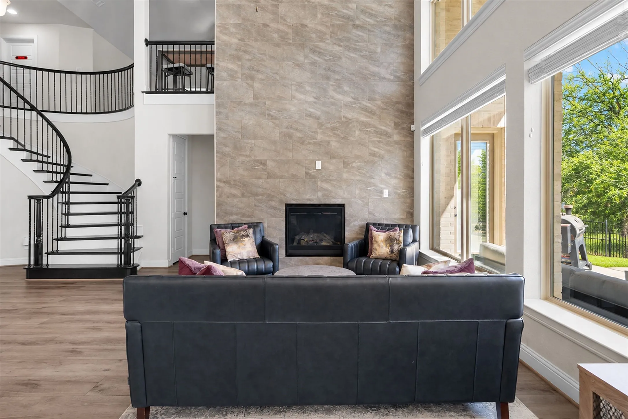 Two-story living area featuring wood-finish flooring, a contemporary fireplace with a stone-clad surround, and a curved staircase with black iron balusters
