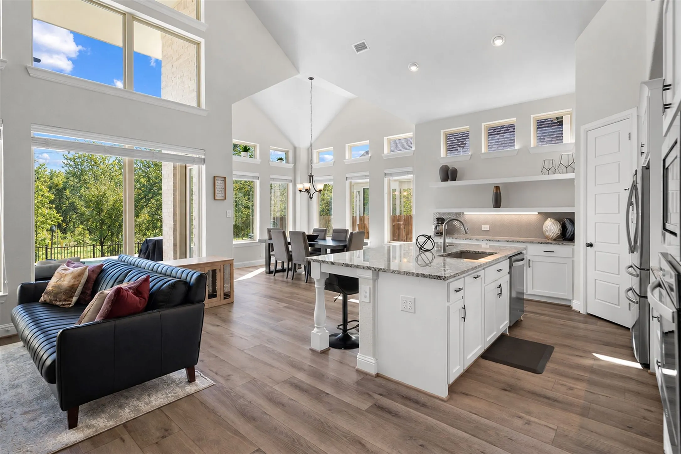 Wood-finish flooring throughout, vaulted ceiling, recessed lighting, white cabinetry, and a kitchen island with a granite countertop