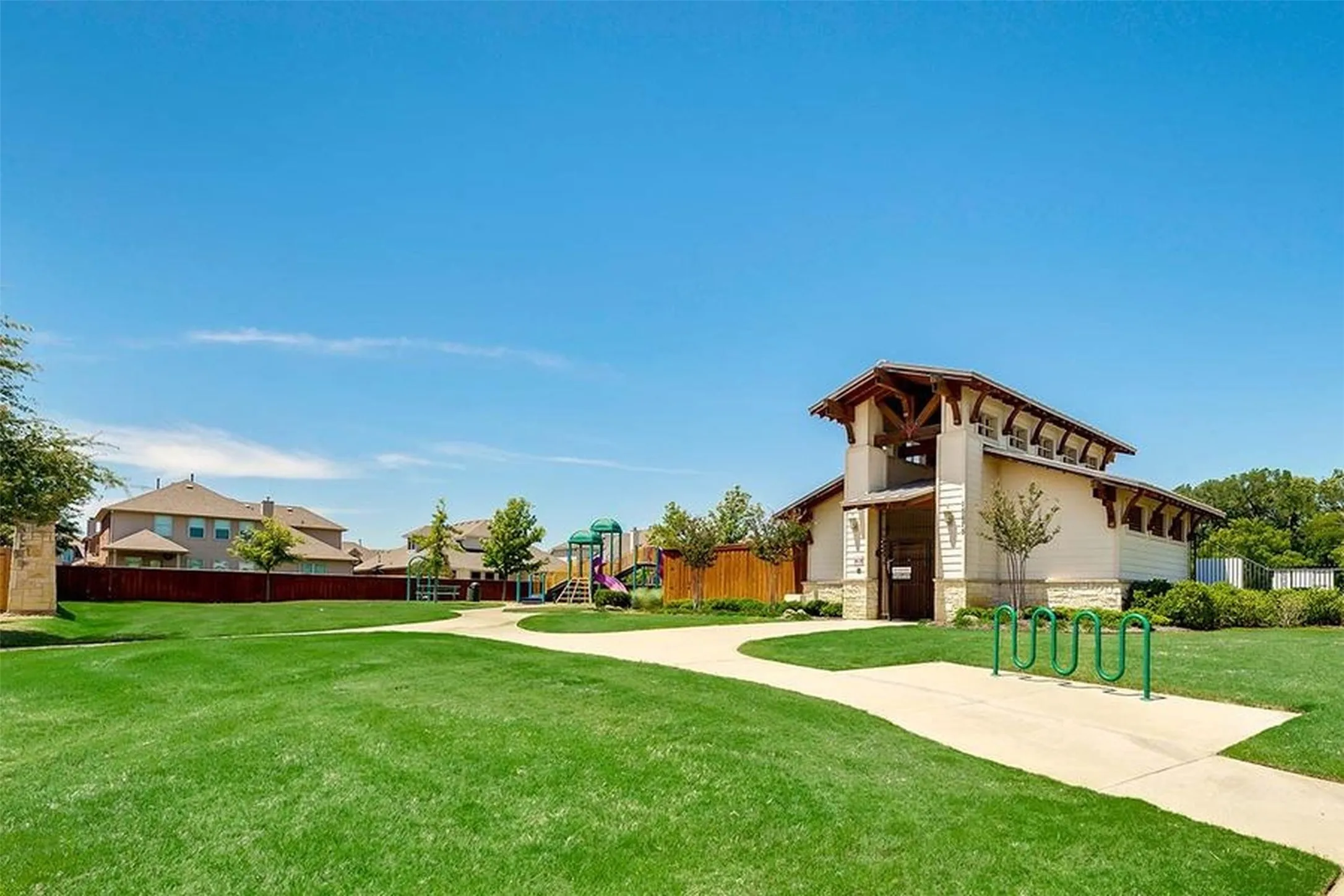 Expansive green space featuring a concrete pathway, a recreational building with exposed wooden beams, and a playground