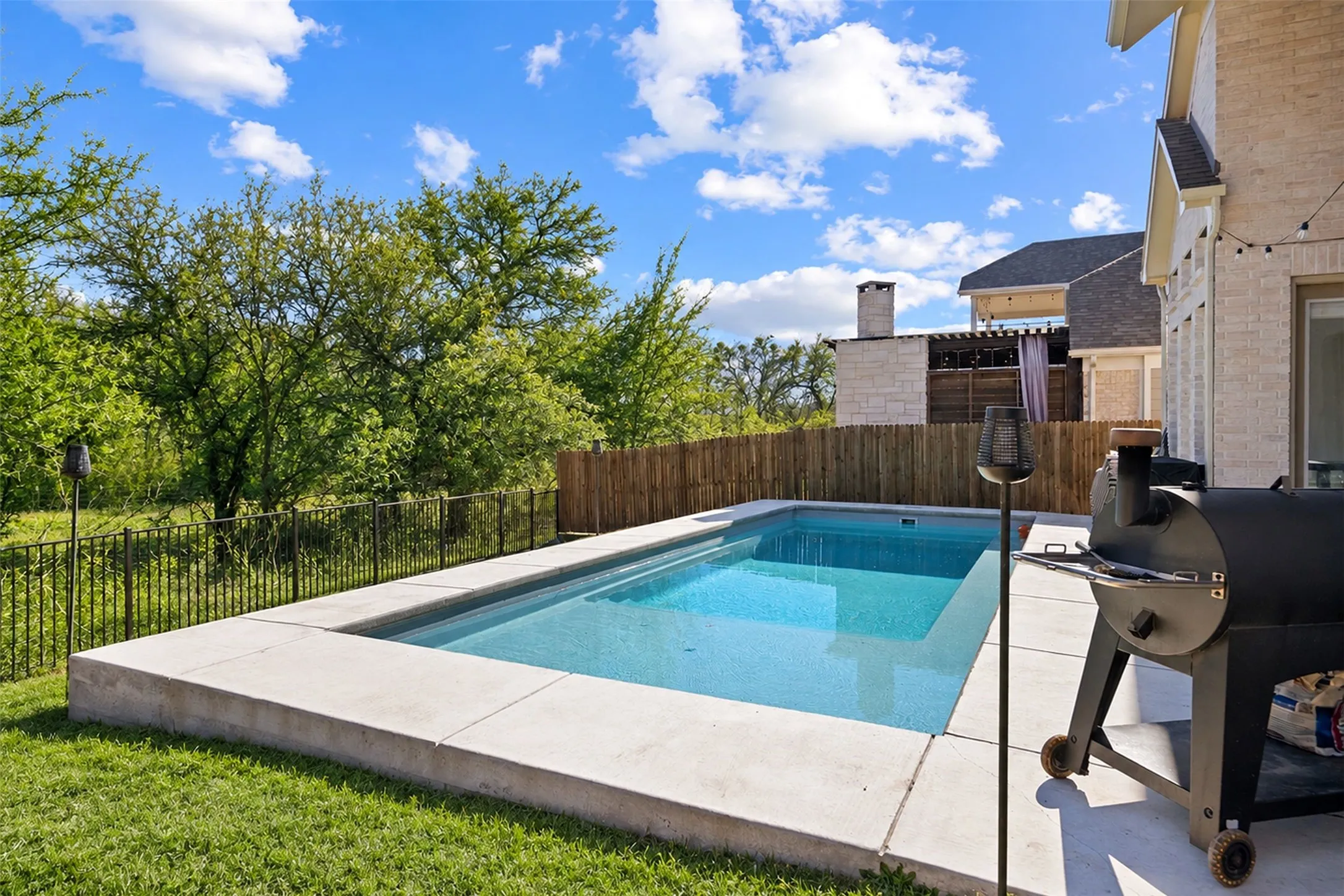 Backyard featuring a rectangular swimming pool with a concrete surround, a wood fence, and a black metal fence