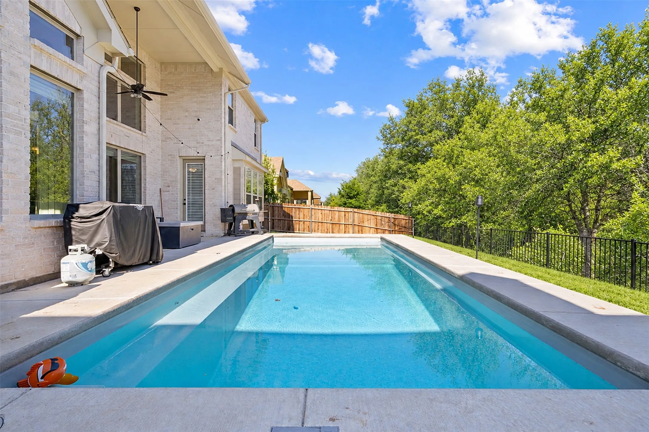 Elongated rectangular swimming pool with integrated steps, surrounded by a concrete patio and a white brick exterior
