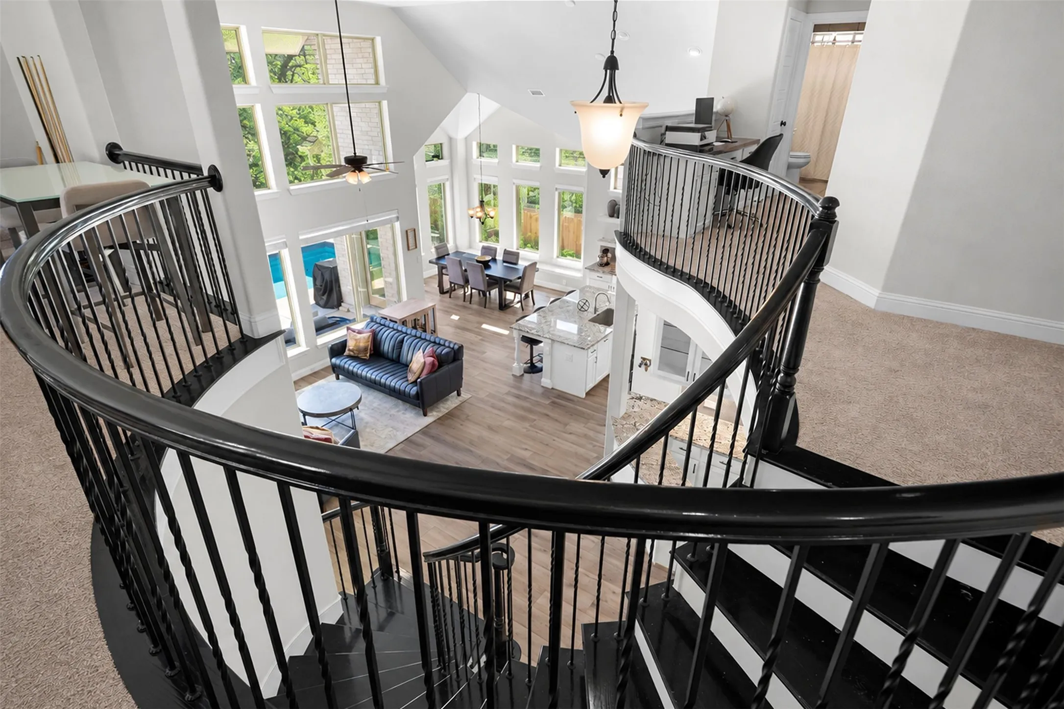 Curved staircase with black railings, vaulted ceiling, extensive window array, wood-finish flooring, and a kitchen island with seating