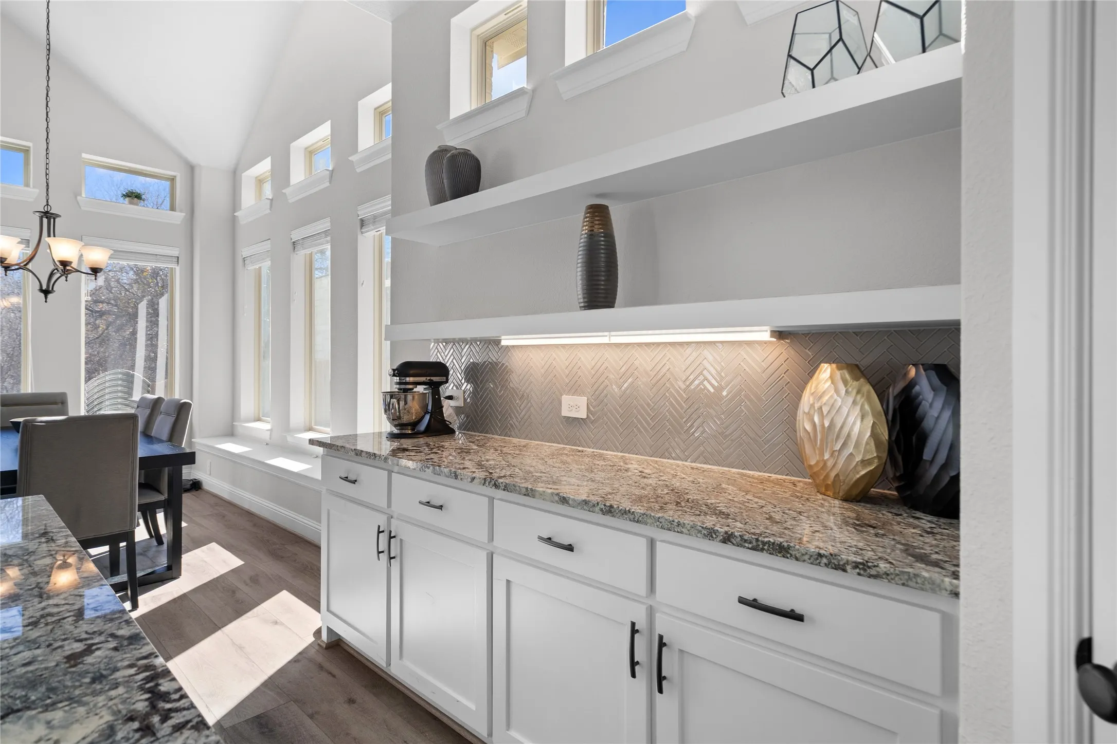 White shaker-style cabinetry with matte black hardware, stone-finish countertops, and under-cabinet lighting