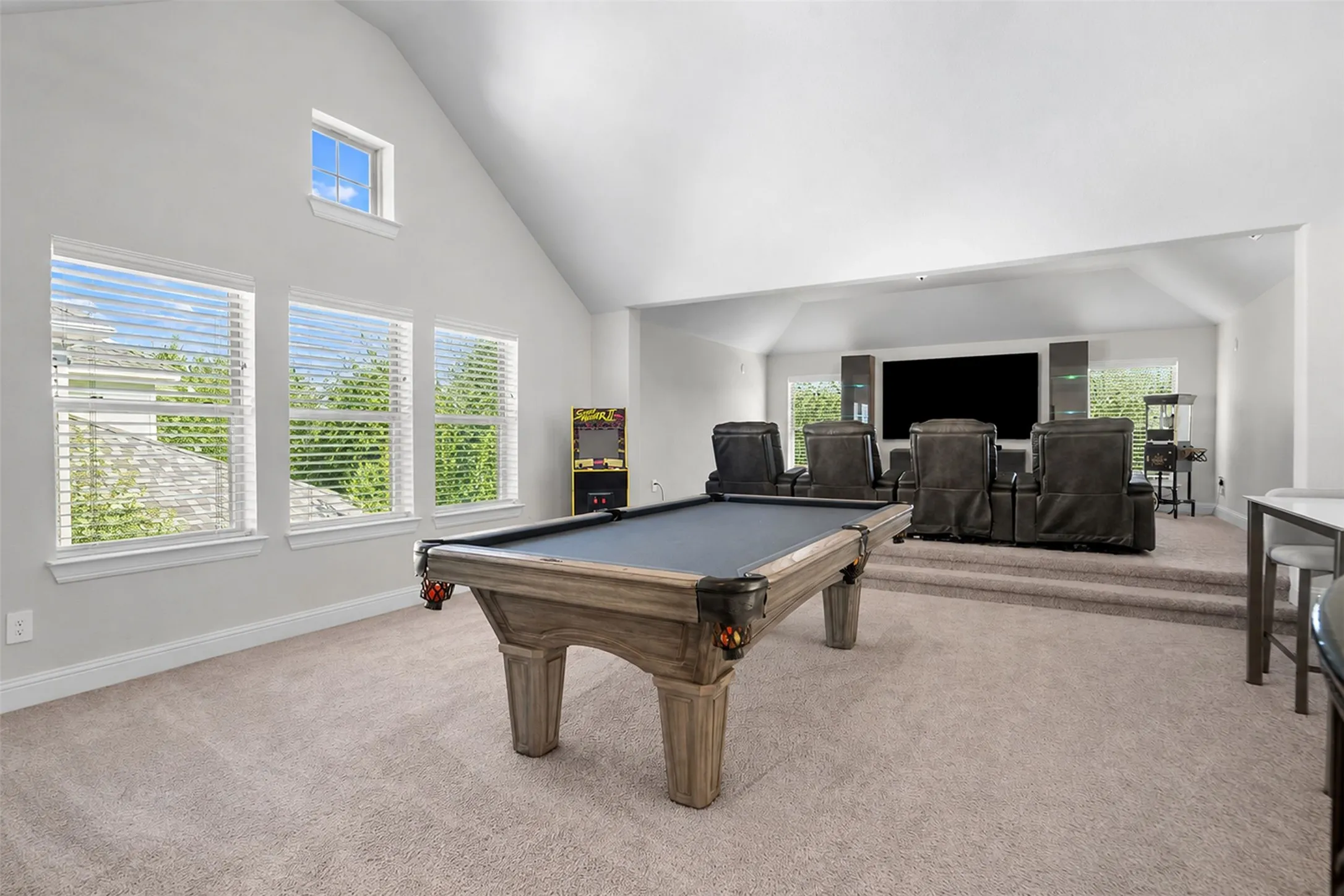 Vaulted ceiling, multiple windows with blinds, carpeted flooring, elevated media area, and a built-in bar table