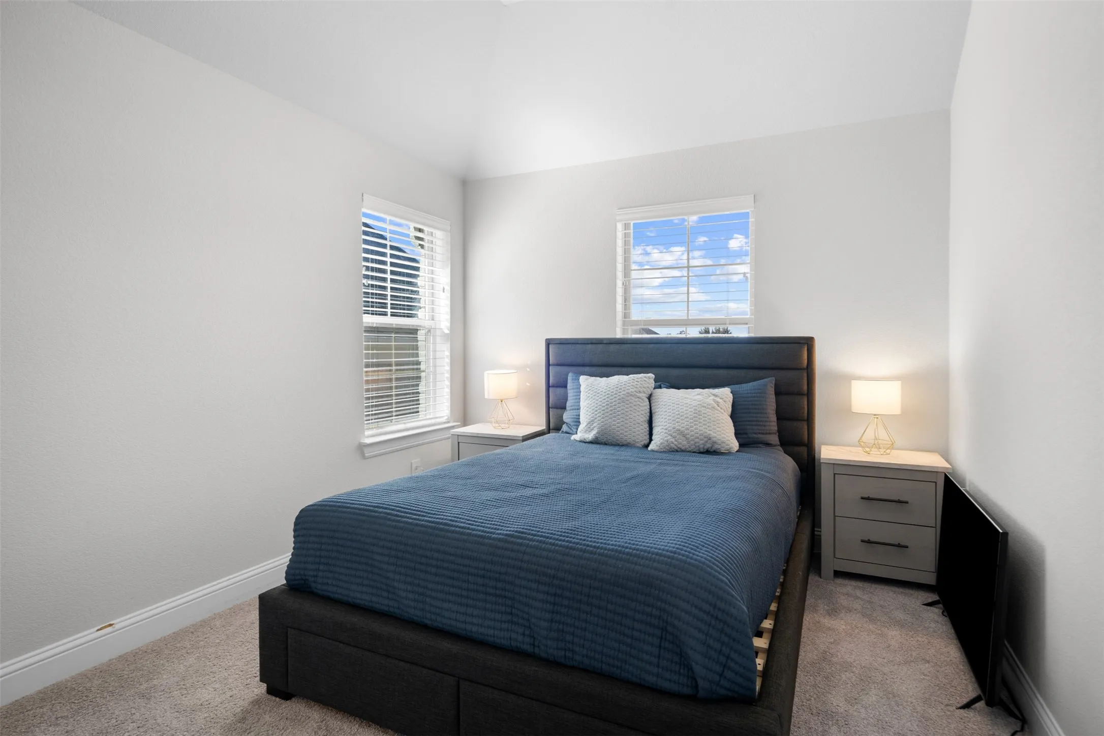 Vaulted ceiling, two windows with blinds, light gray walls, and carpet flooring