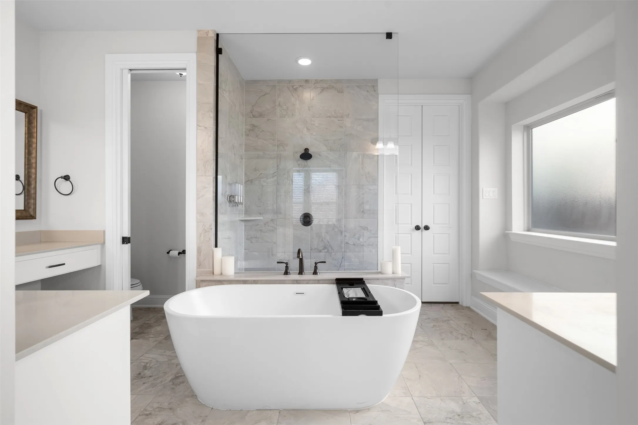 Freestanding soaking tub, walk-in shower with glass enclosure, dual vanity with undermount sinks, tile flooring, and a large window with a built-in bench