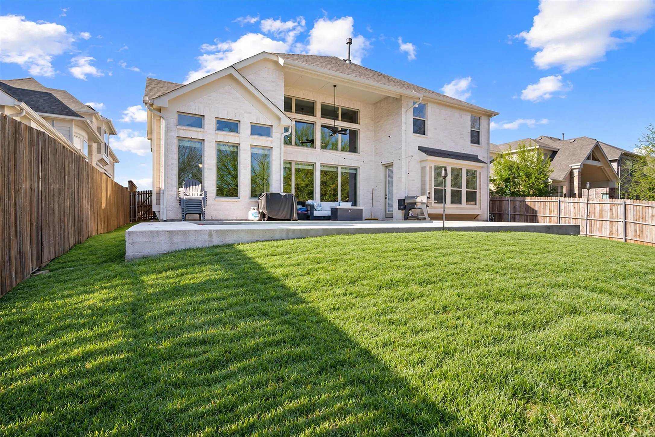 Expansive backyard featuring a manicured lawn, concrete patio, and privacy fencing