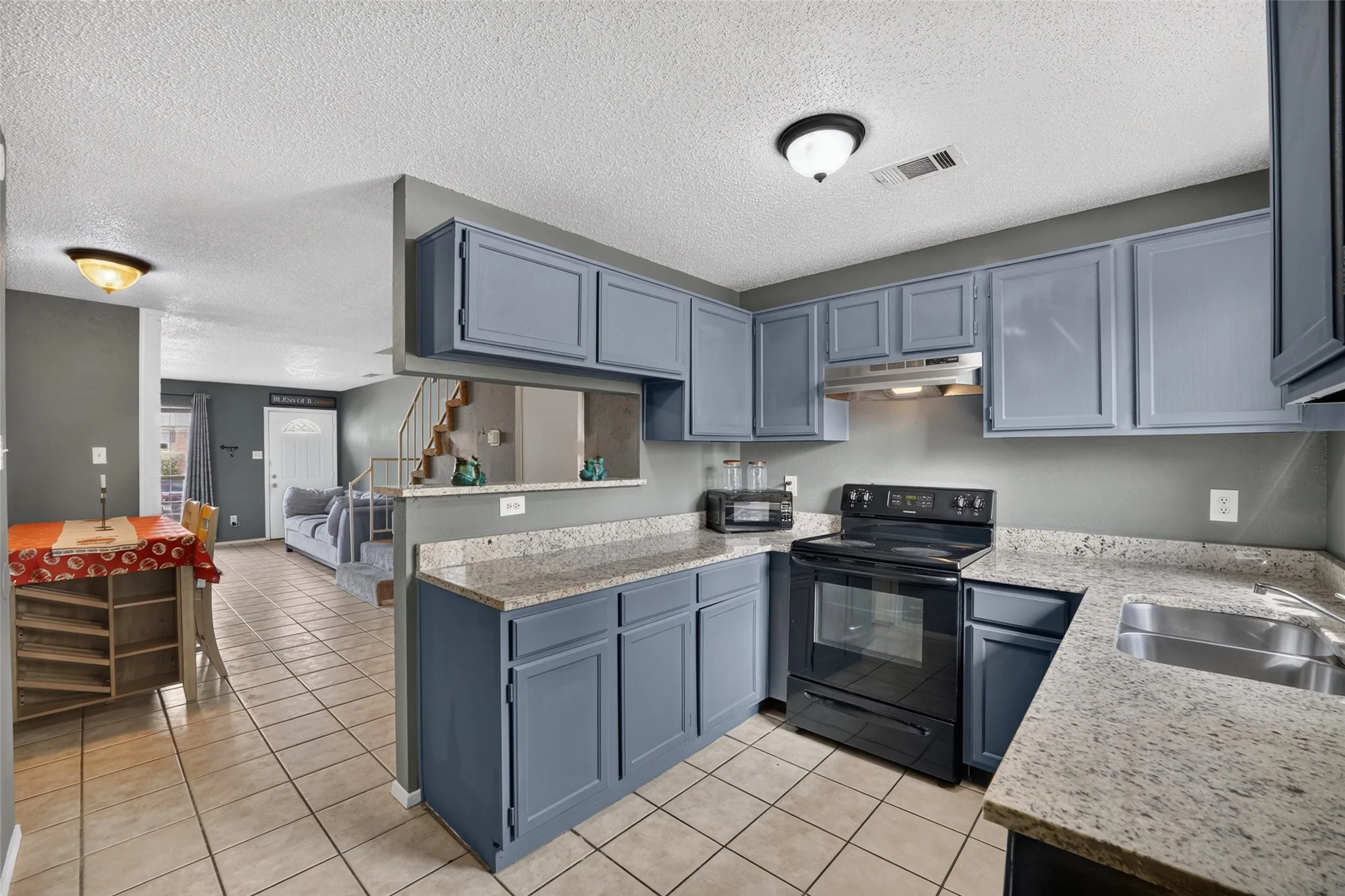 Kitchen featuring blue cabinetry, light-toned countertops, a black electric range, and a stainless steel sink