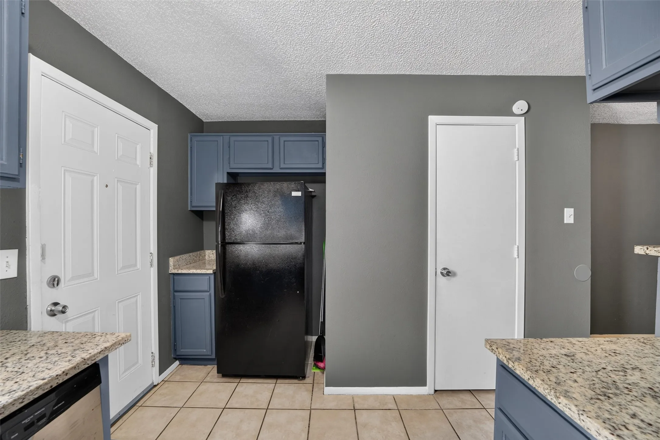 Spacious kitchen featuring granite-style countertops, stainless steel appliances, blue cabinetry with traditional paneling, tile flooring, and ample counter workspace